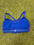 Front view of vibrant blue Sweaty Betty sports bra with thin straps and elastic underband on grass