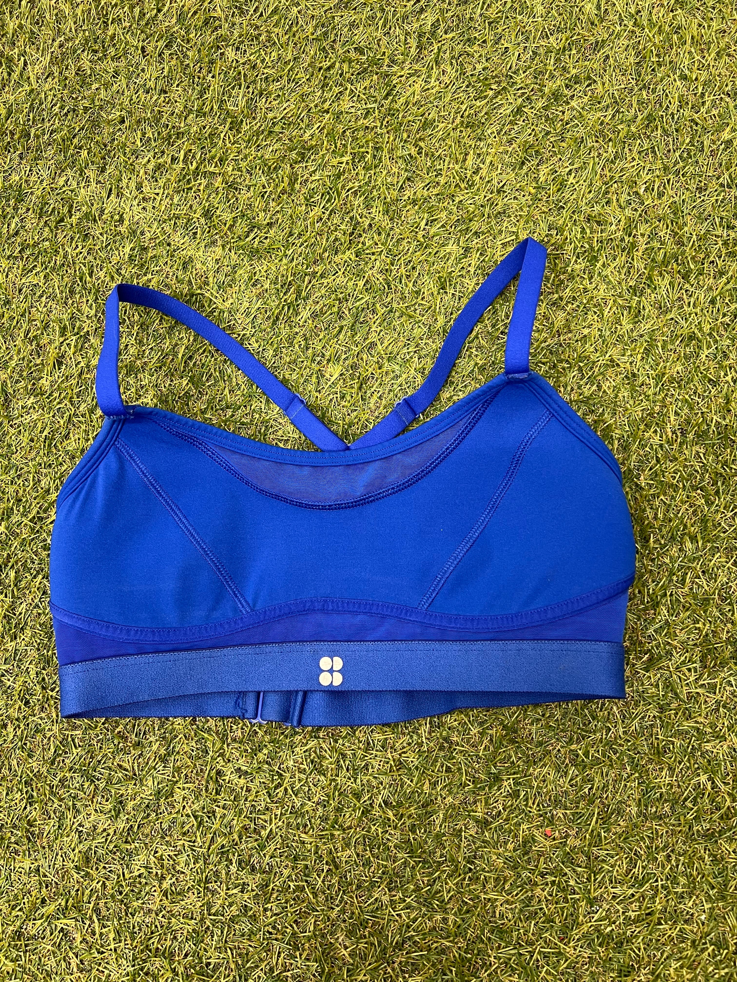 Front view of vibrant blue Sweaty Betty sports bra with thin straps and elastic underband on grass