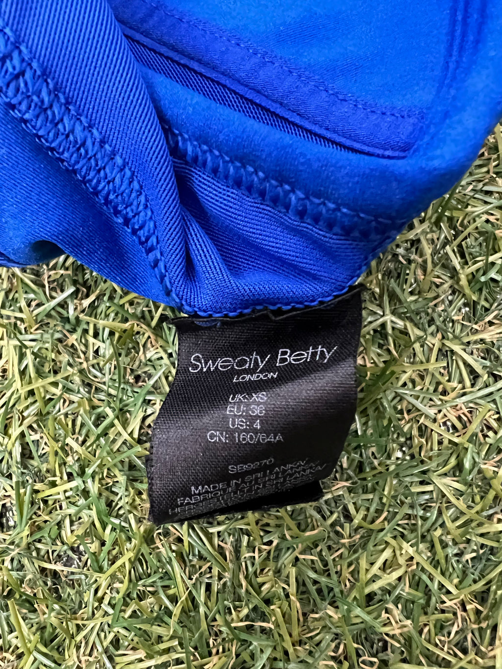 Close-up of black clothing tag on blue sports bra top showing Sweaty Betty branding and size XS
