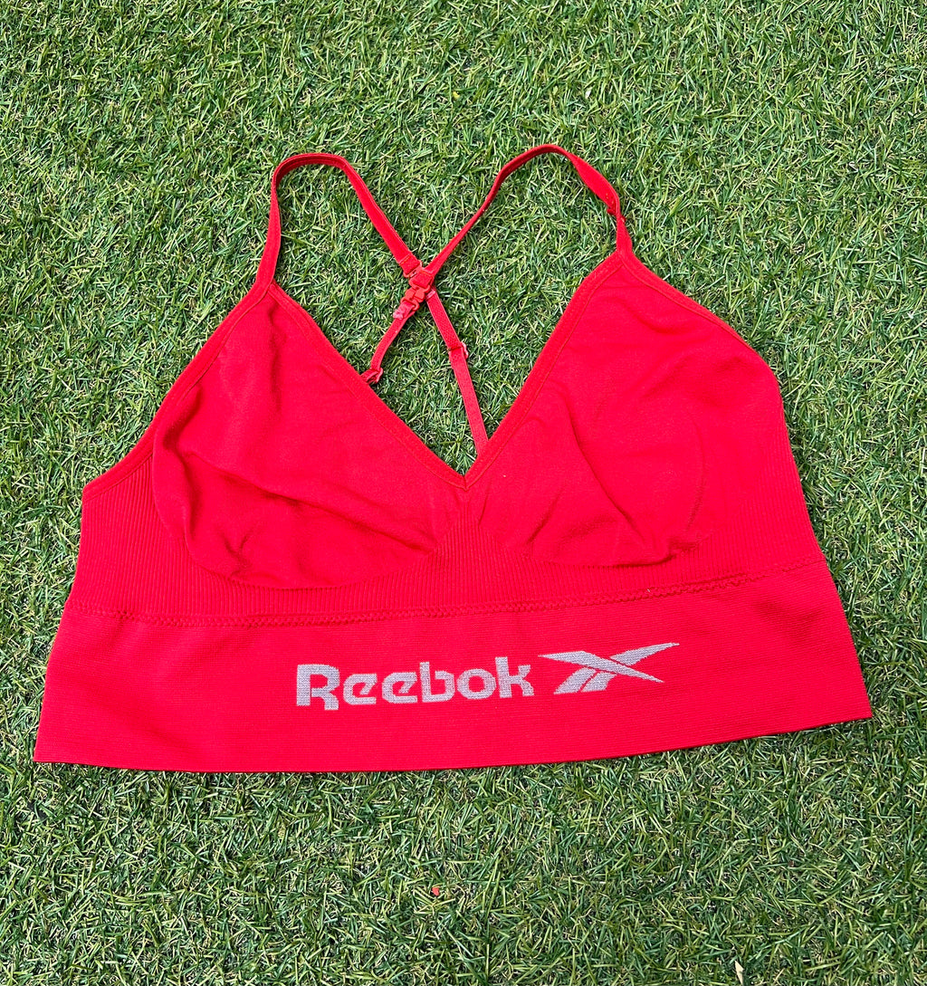 Front view of red Reebok sports bra top laid flat on grass showing logo and adjustable straps