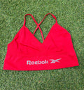 Front view of red Reebok sports bra top laid flat on grass showing logo and adjustable straps