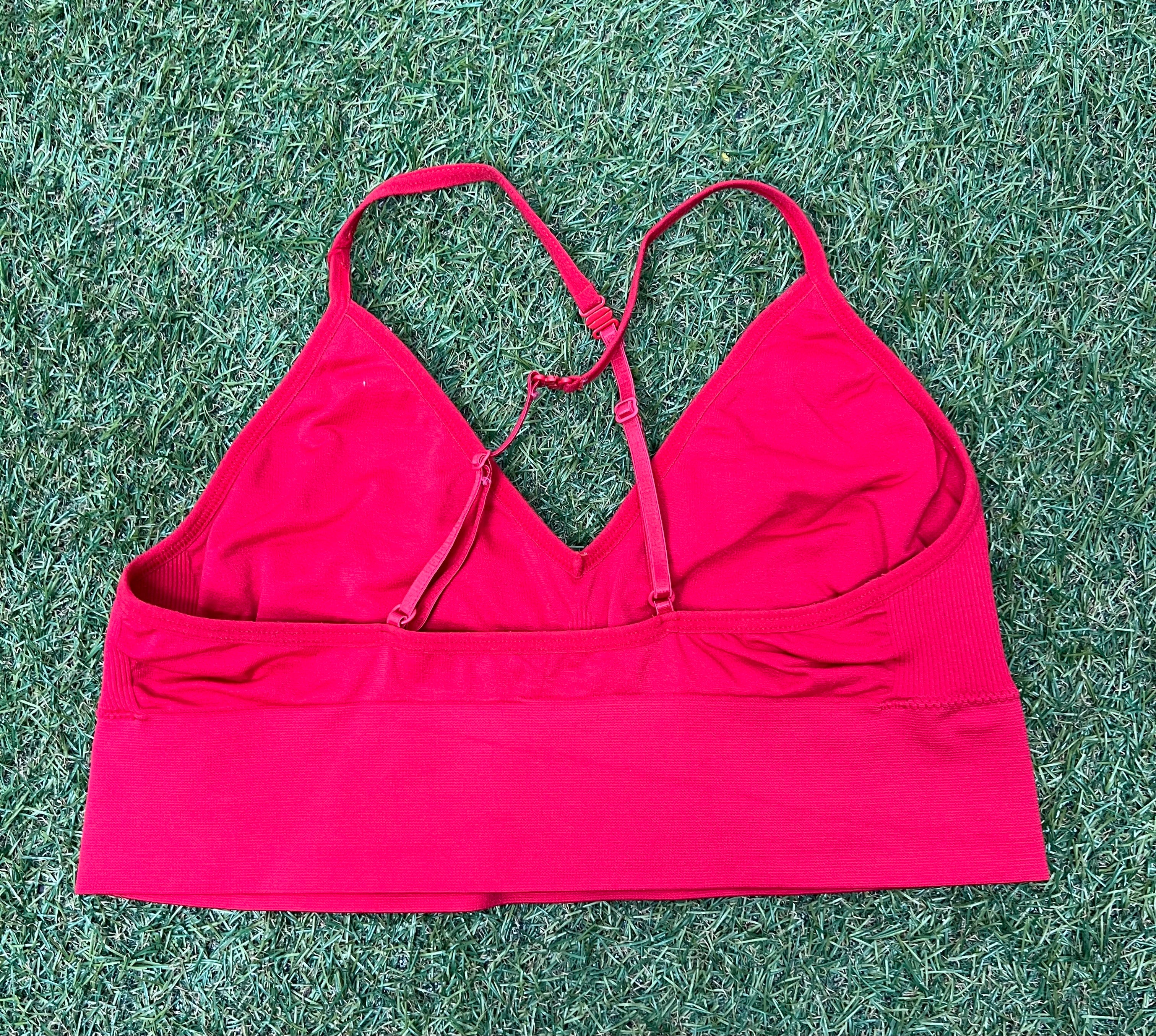 Back view of red Reebok sports bra top with crossed adjustable straps visible against grass