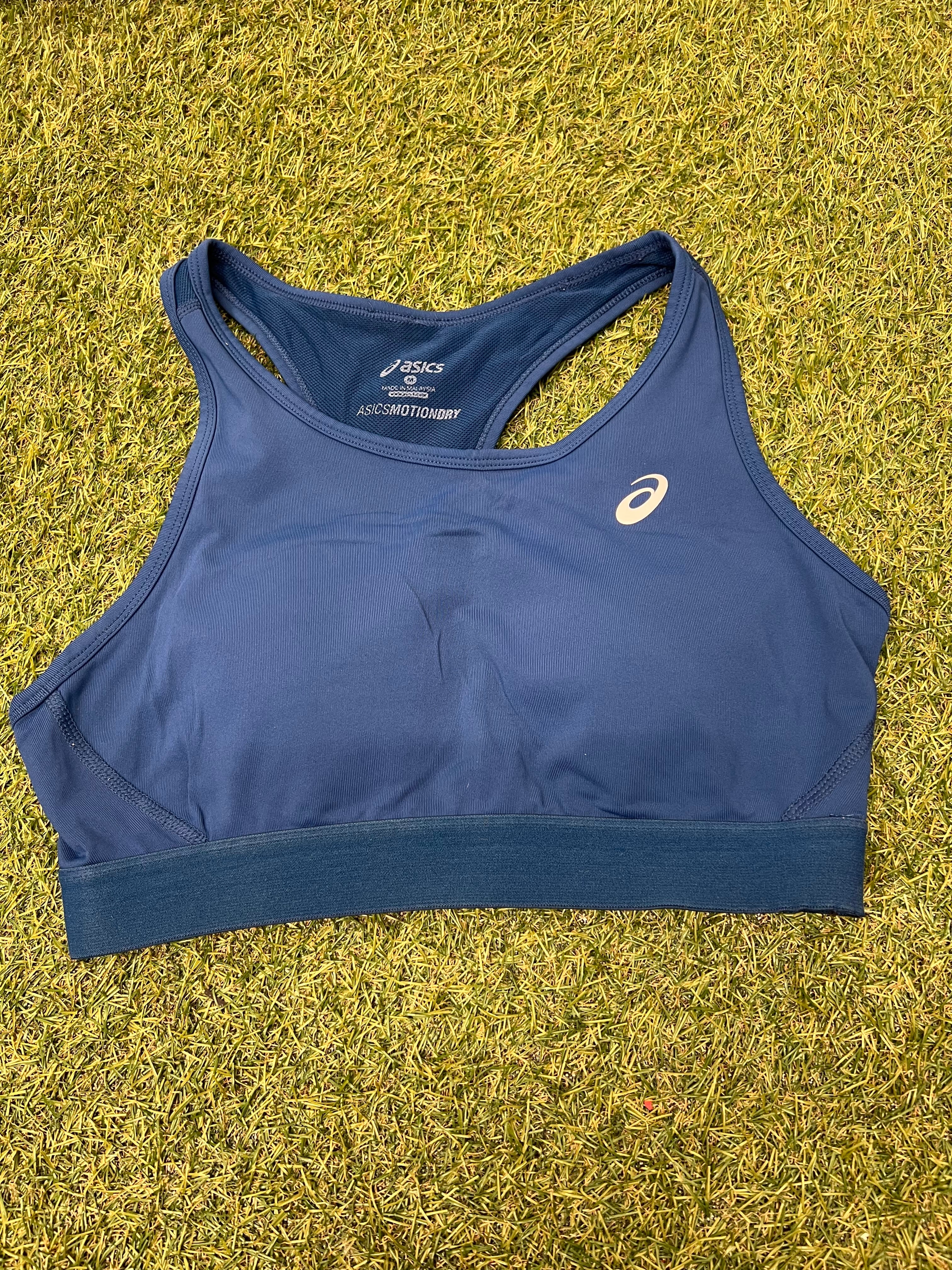 Front view of Asics blue sports bra laid flat on grass