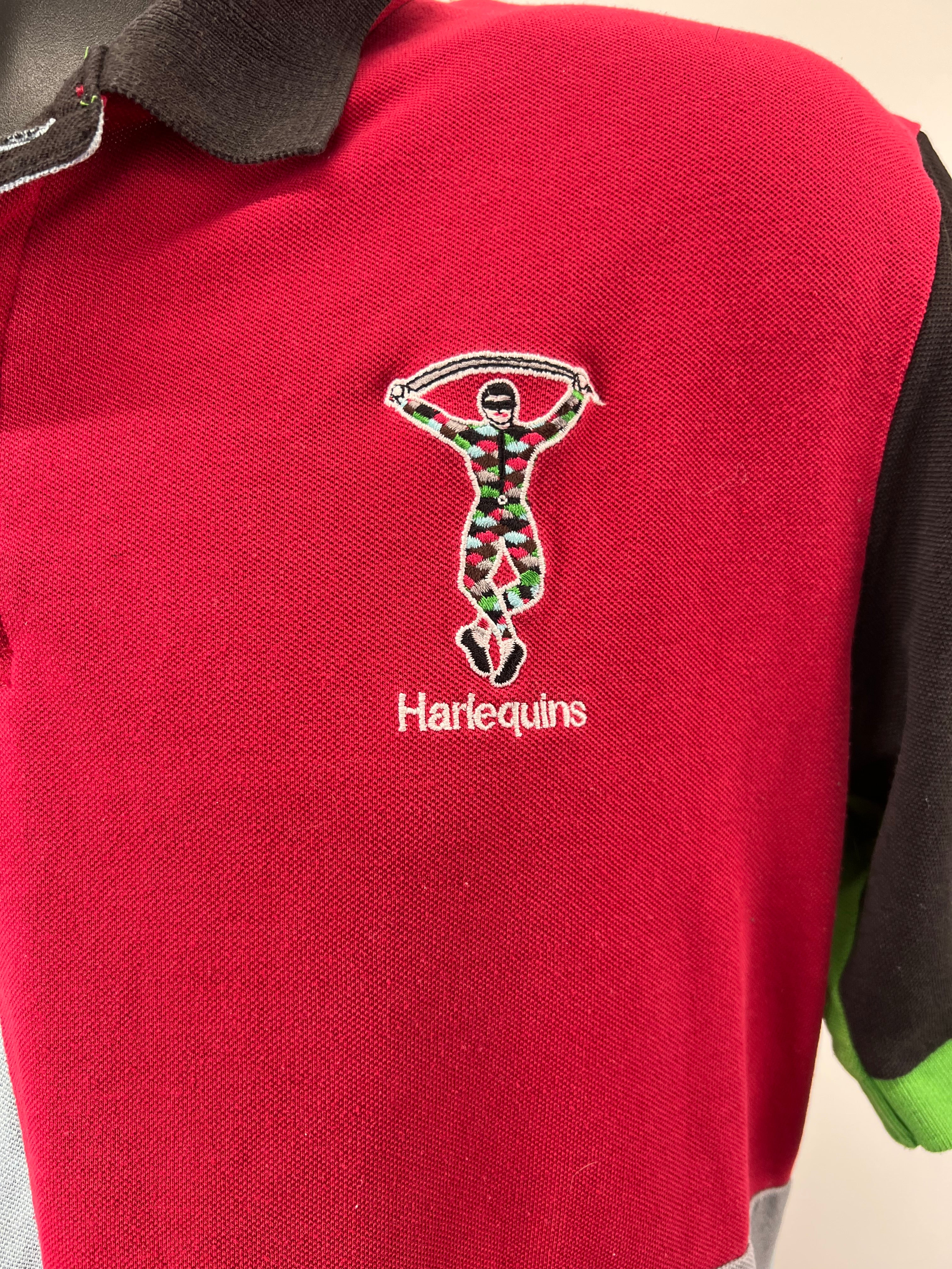 Close-up of the embroidered Harlequins jester logo on the red chest panel of the polo shirt