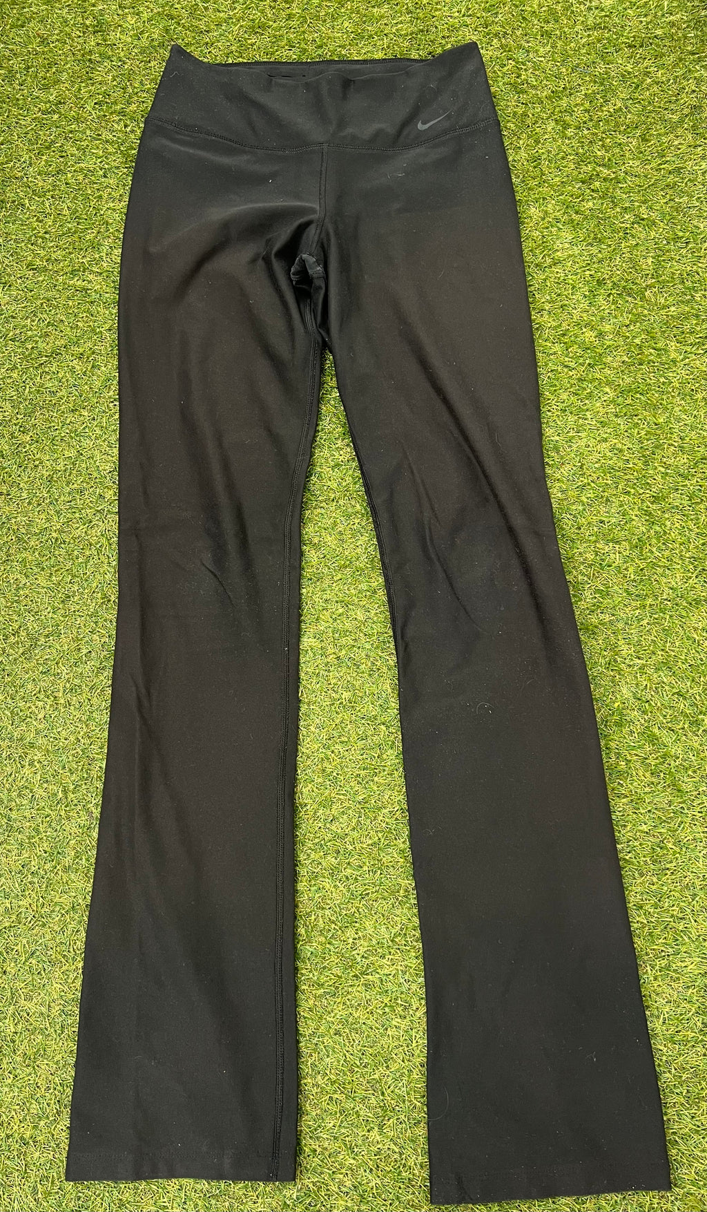 Front view of women's black Nike Dri-FIT leggings laid flat on grass surface