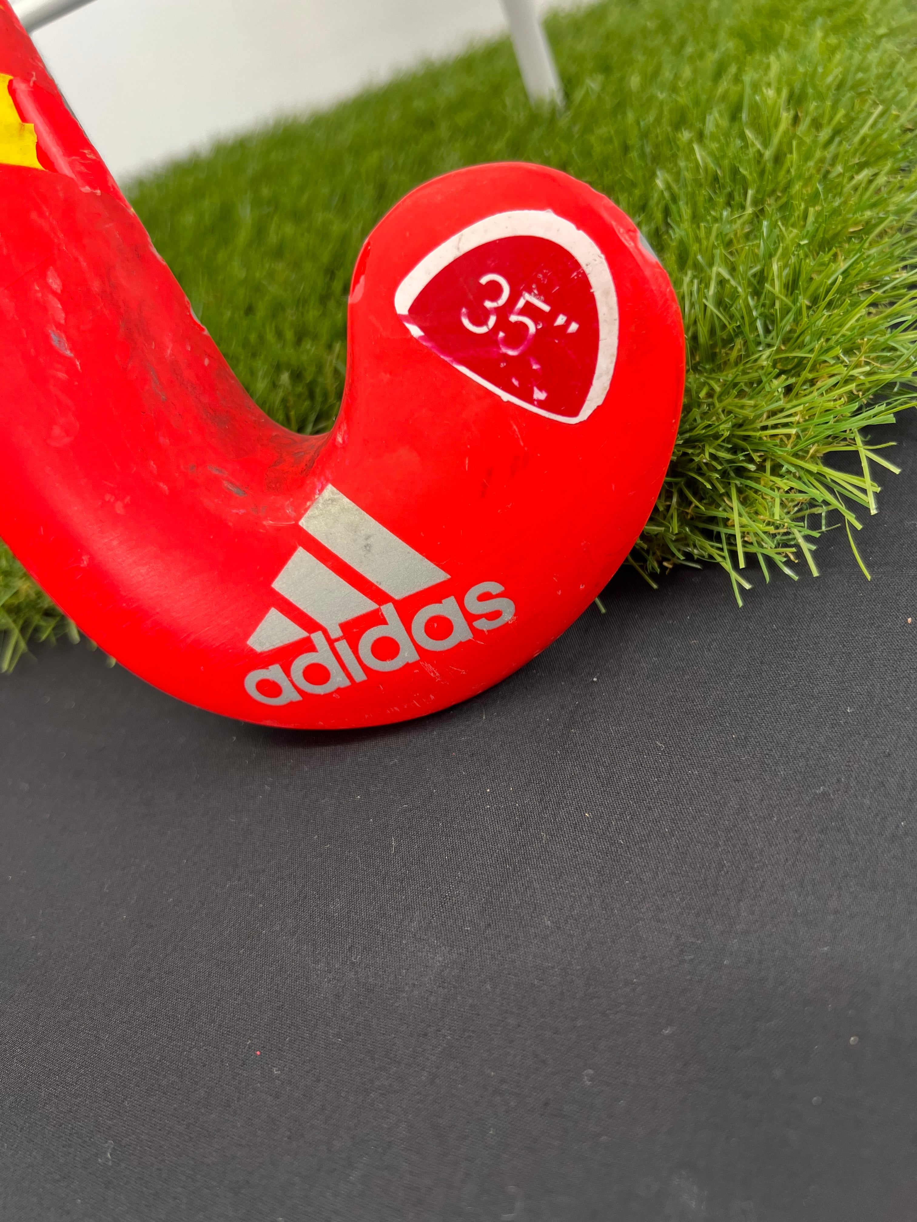 Close-up of the curved end of the stick showing adidas logo and 35 inch marking on red surface with scrapes