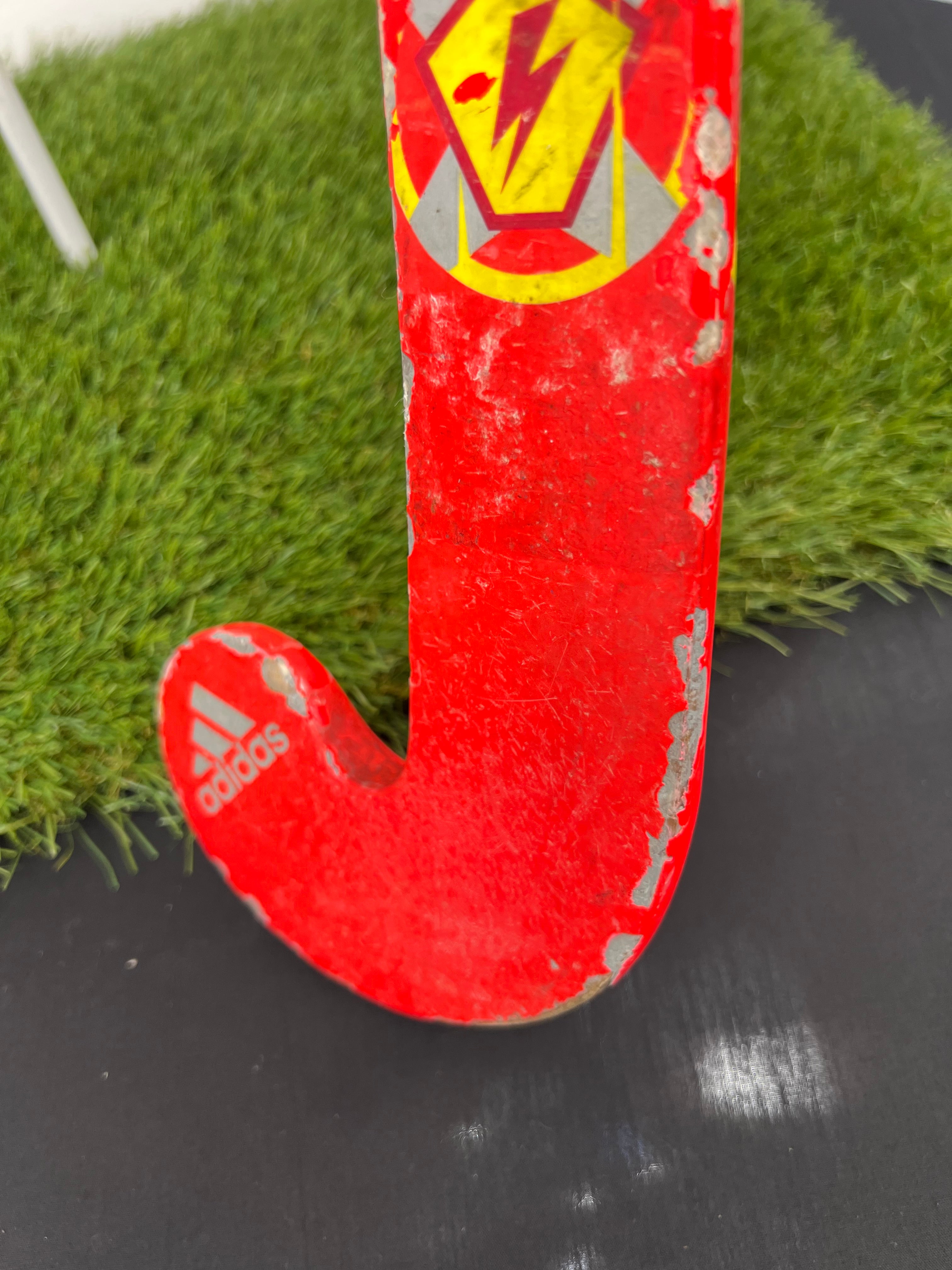 Detailed worn area along the curved toe of the stick showing scuffs and paint chips on the red surface