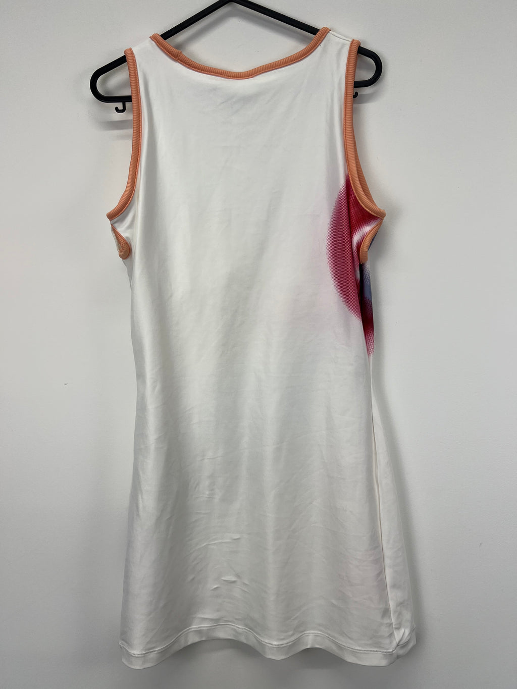 Back view of white Nike tennis dress showing plain white back and peach-coloured trims on a black hanger