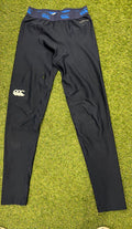 Front view of Canterbury navy base layer leggings laid flat on grass, featuring elastic waistband with blue logos
