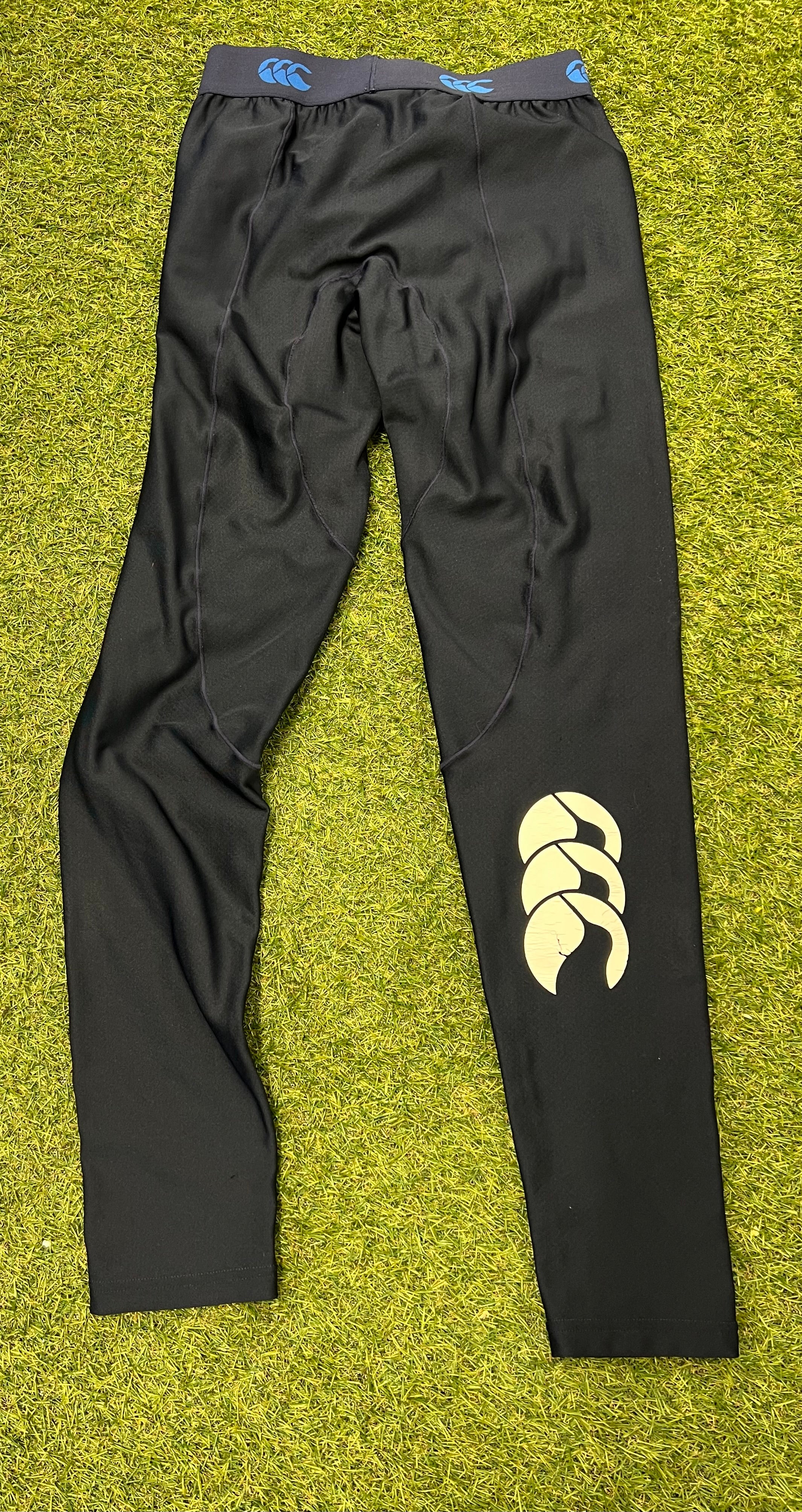 Back view of Canterbury navy base layer leggings on grass, showing ergonomic seams and large Canterbury logo on calf