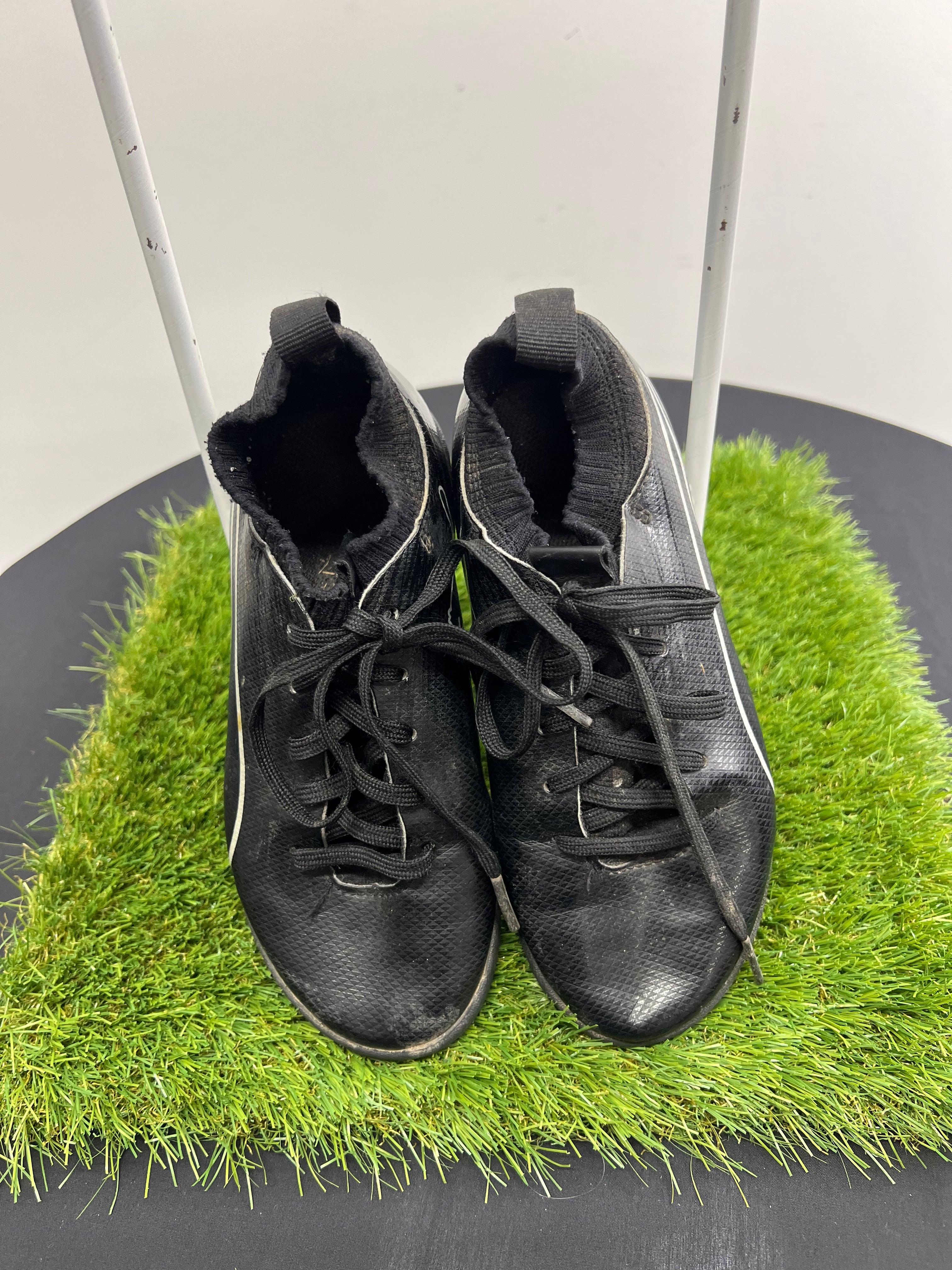 Top view of black Kids Puma Astro turf football boots with laces on green artificial grass