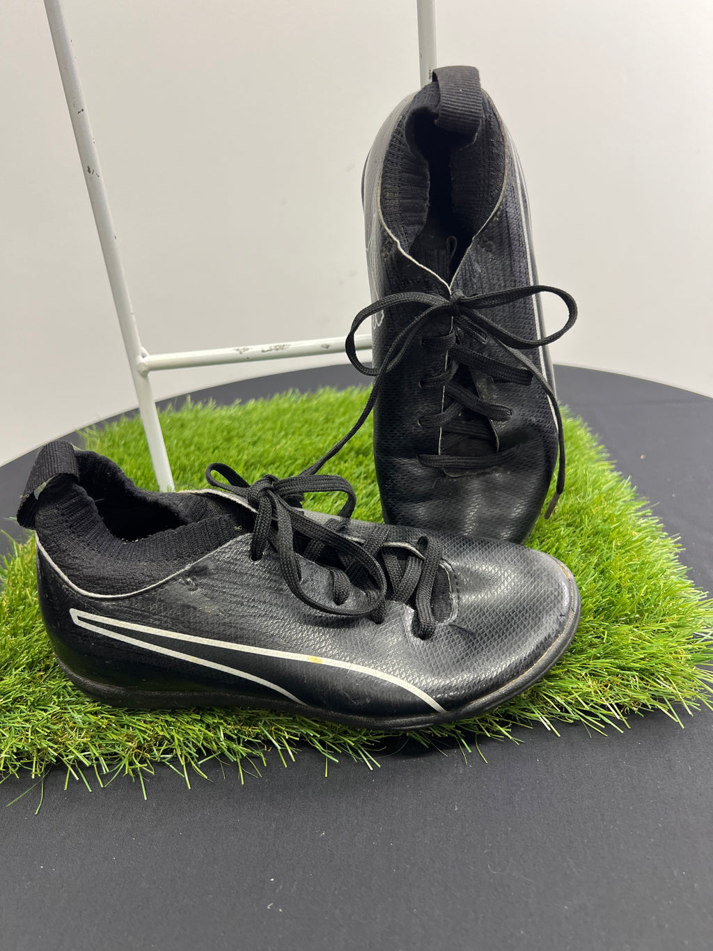 Side angle of black Puma football boots with white logo and sock-like ankle collar on turf