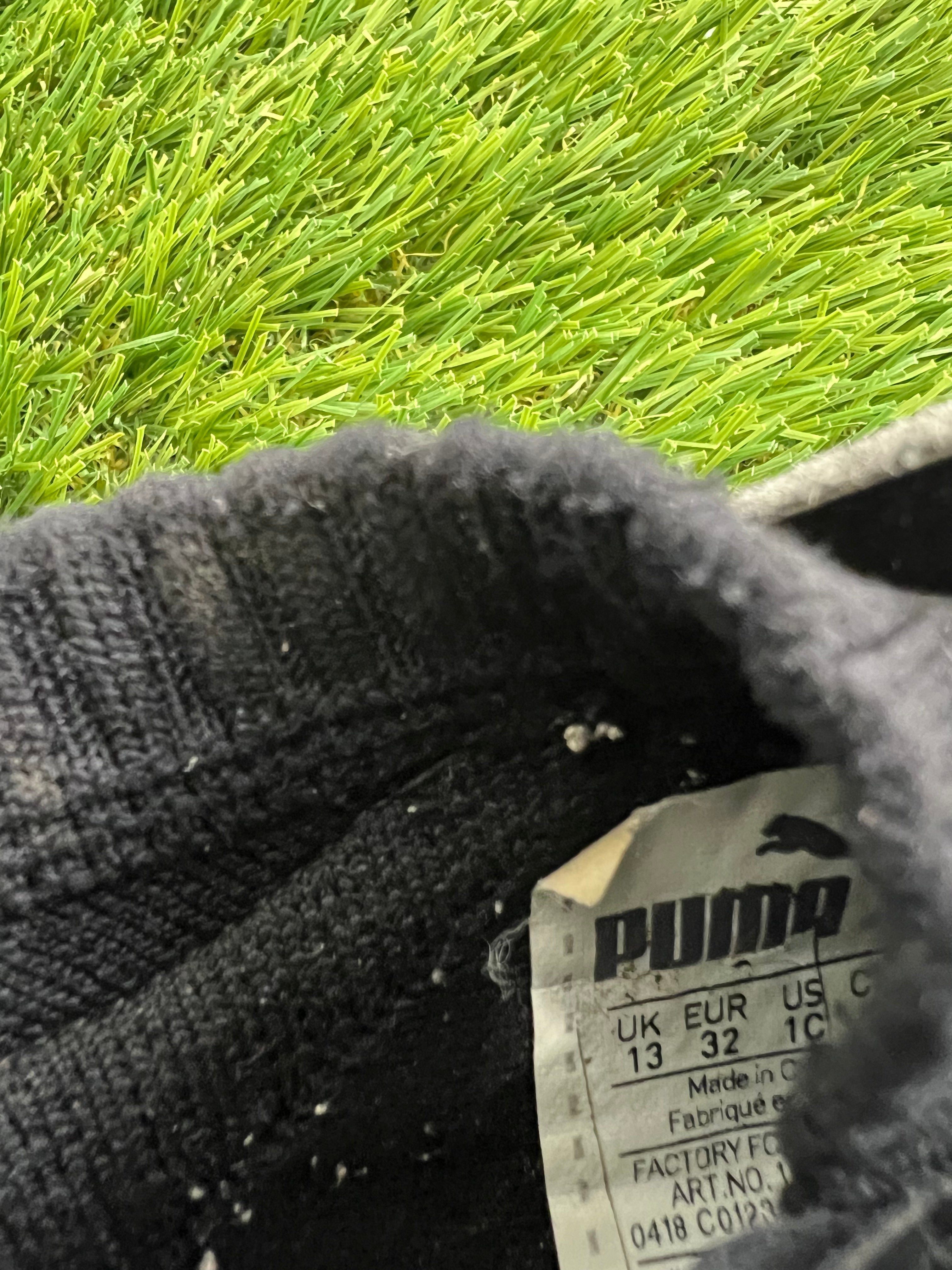 Pair of black Puma Astro turf football boots displayed on green synthetic grass surface