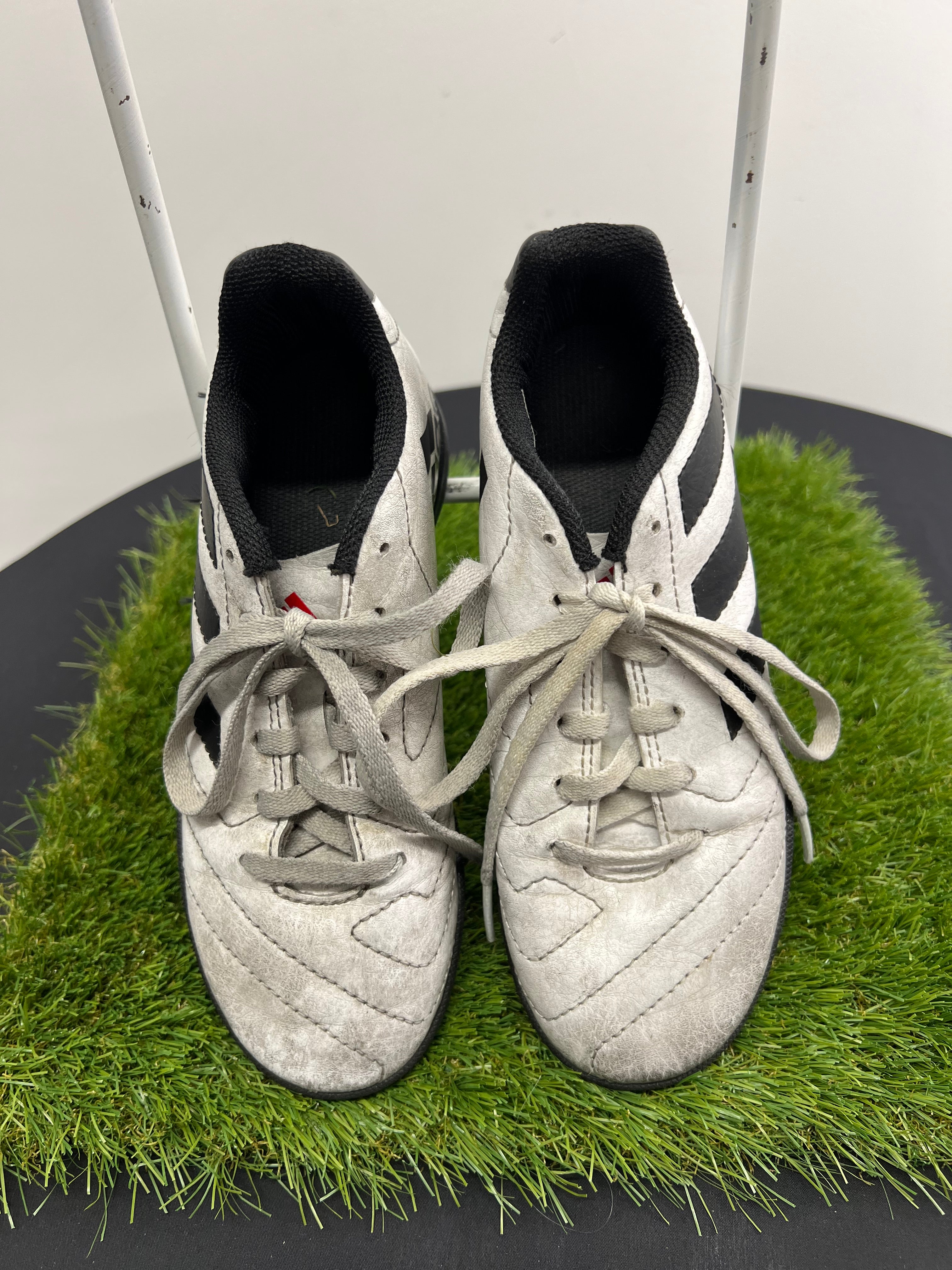 Front view of kids adidas Astro turf football boots in white and black with tied laces on grass
