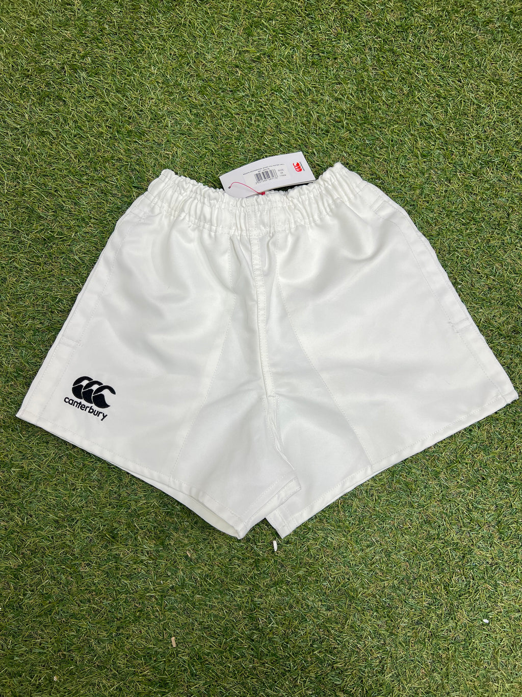 Front view of white Canterbury kids' twill shorts with elastic waistband on grass