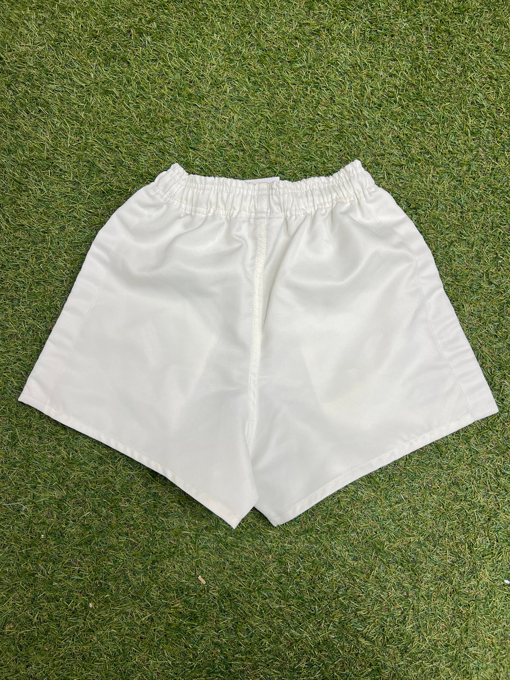 Back view of white Canterbury kids' twill shorts displayed on grass