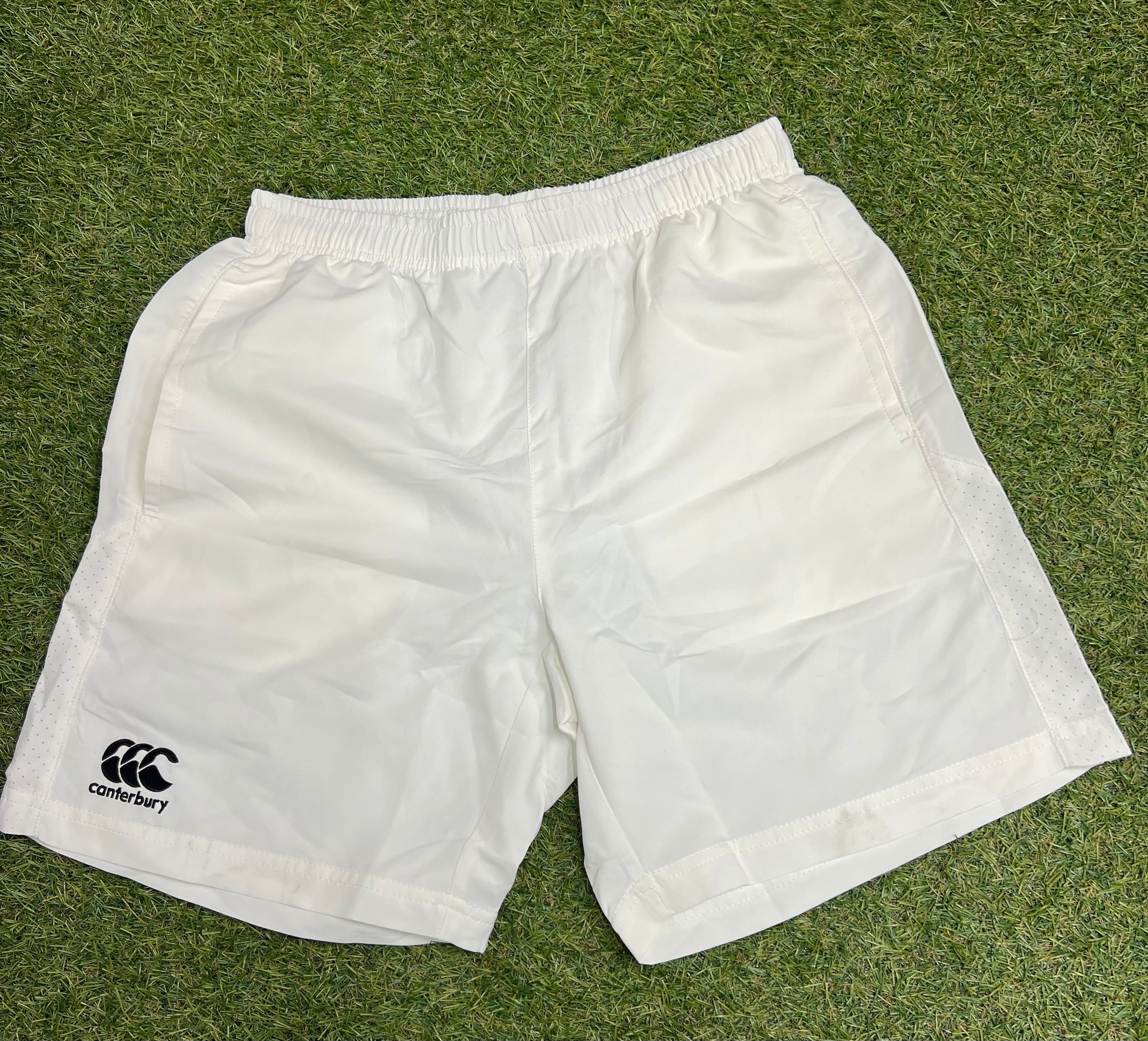 Front view of men’s Canterbury white team sports shorts on grass with elastic waistband and black logo