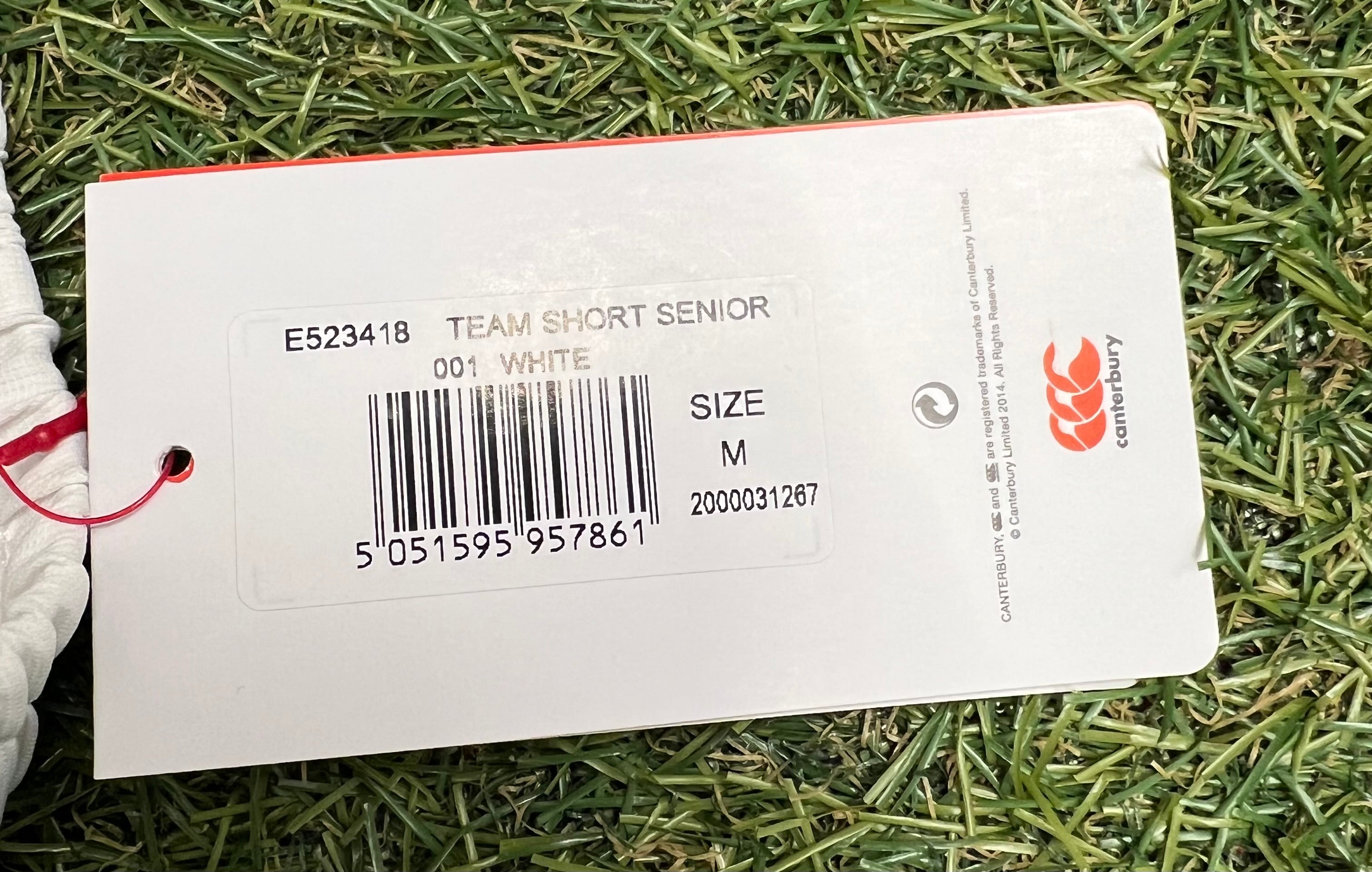 Close-up of Canterbury team shorts white medium tag with barcode on grass