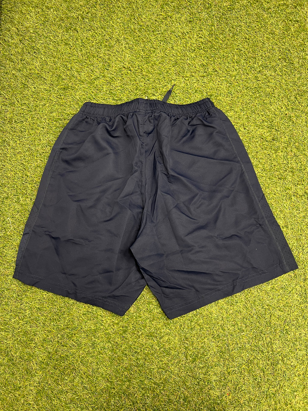 Back view of navy Canterbury men's team shorts displayed on grass surface highlighting perforated side panels
