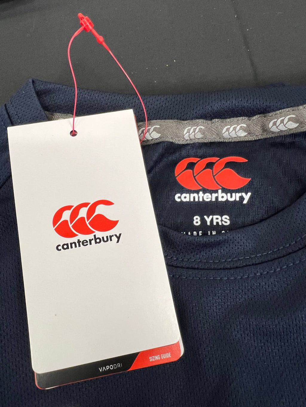 Close-up of Canterbury logo and age 8 label on navy kids sports tee