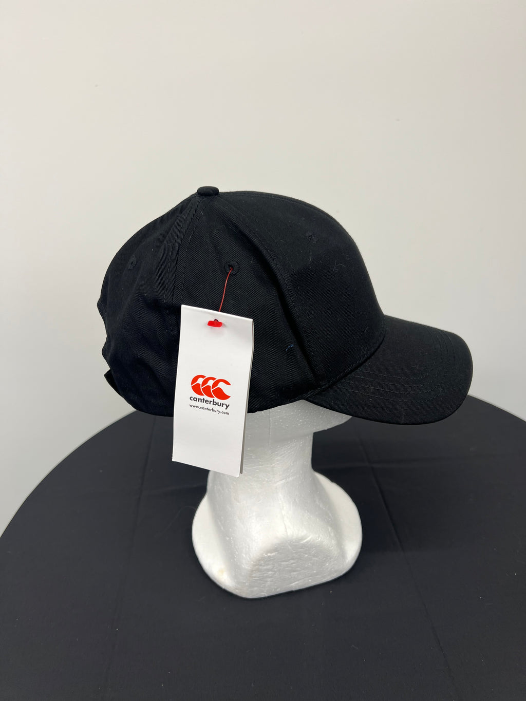 Angled side view of Canterbury black cap with white tag attached