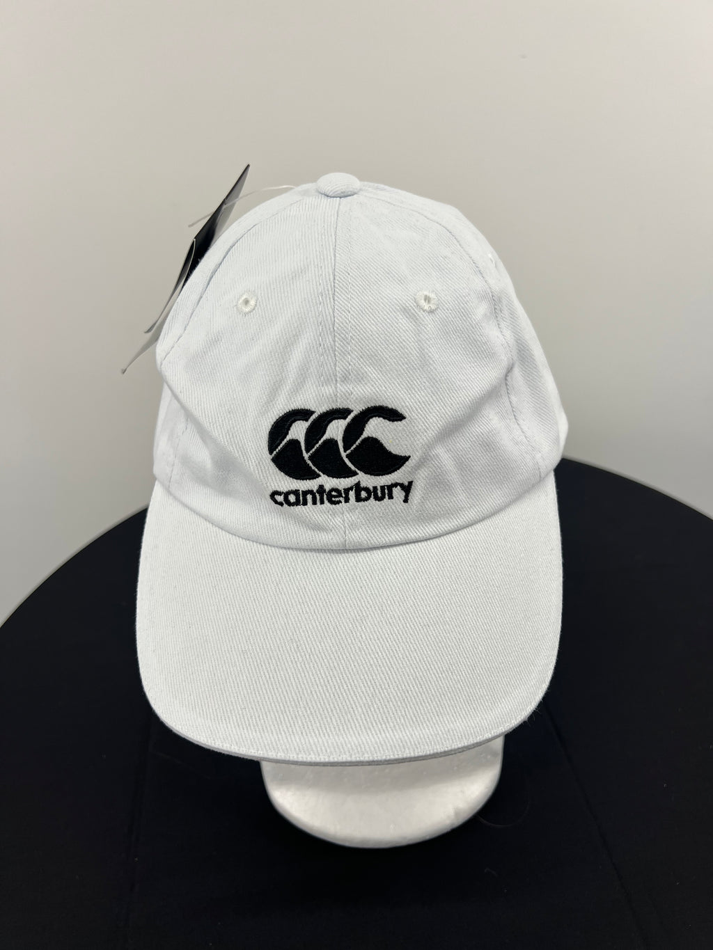 Front view of white Canterbury cap with black embroidered logo on front panel