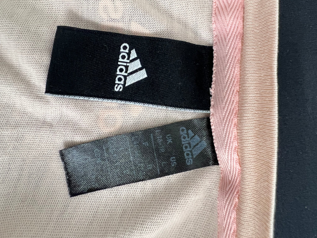 Close-up of Adidas product tags inside pink t-shirt showing size L and brand logo