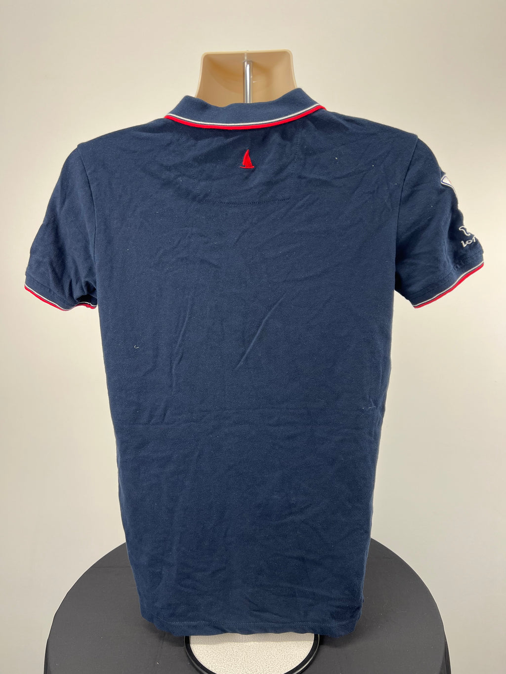 Back view of navy polo shirt showing plain design with small red sail logo under collar