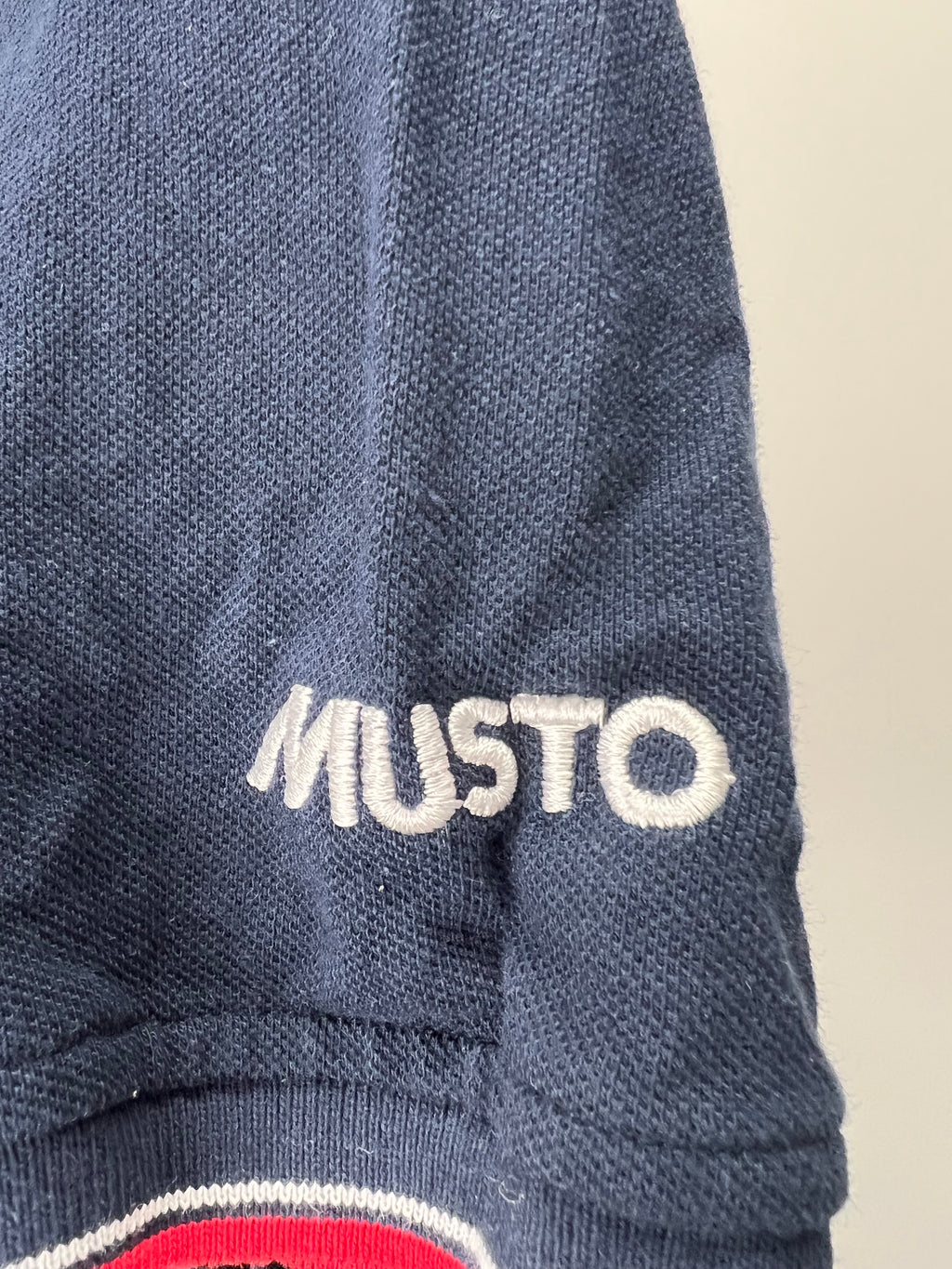 Close-up of sleeve showing embroidered 'MUSTO' logo in white stitching