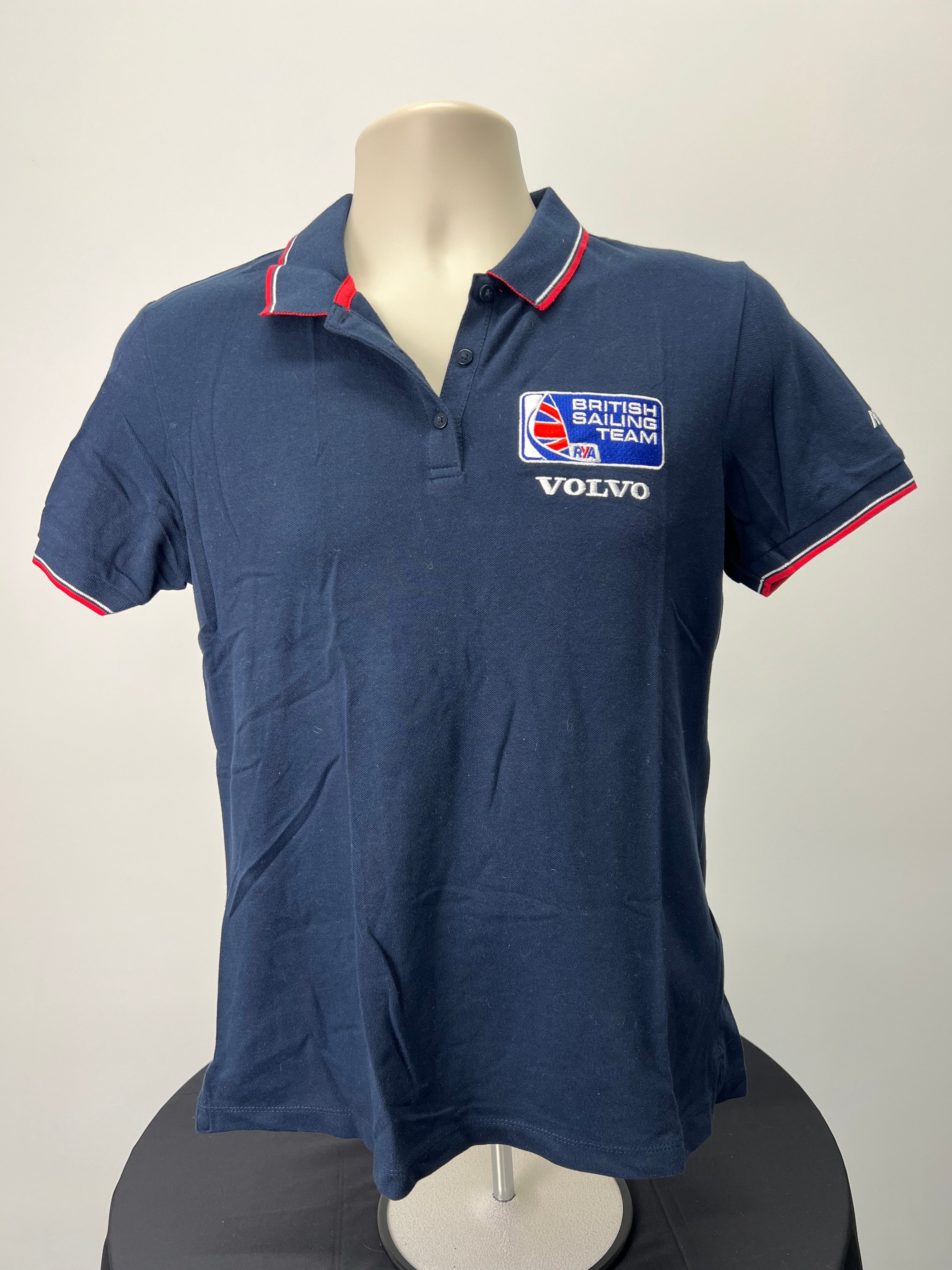 Front view of navy blue Musto British Sailing Team polo shirt with embroidered British Sailing Team and Volvo logos