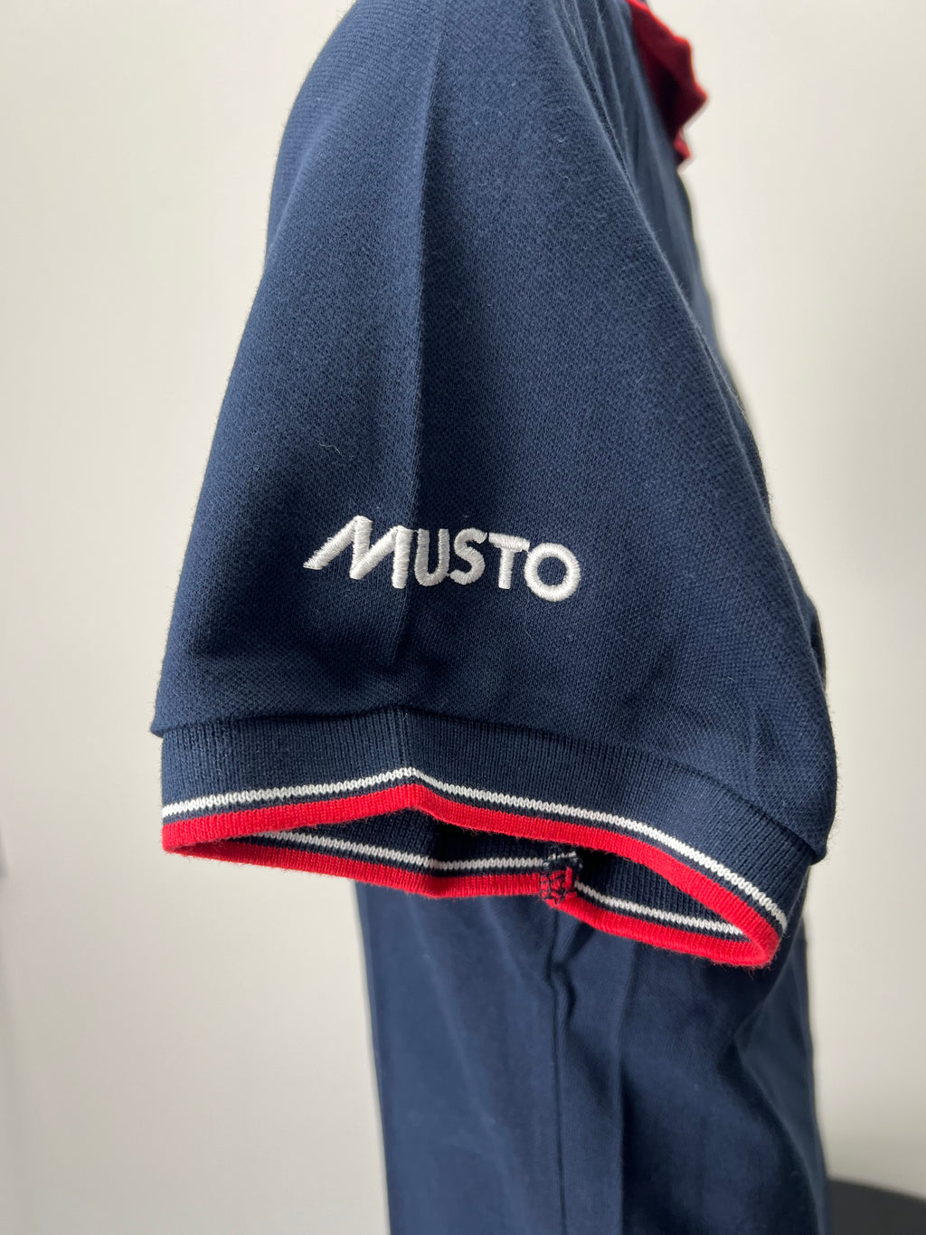 Close-up of polo shirt sleeve featuring Musto logo in white and red and white striped cuff