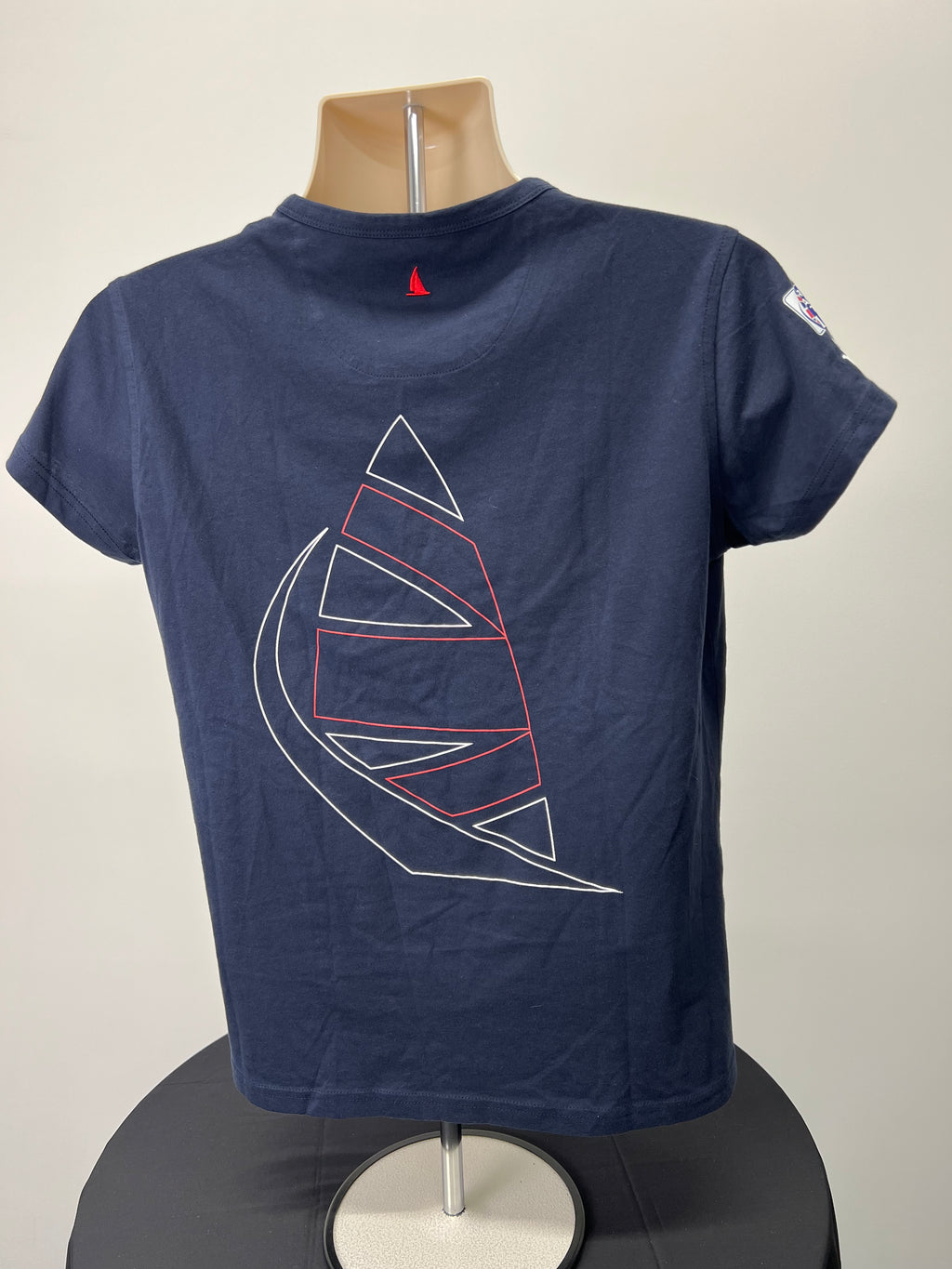 Back view of navy blue t-shirt showing large outlined sail graphic and small red sail embroidered at neckline