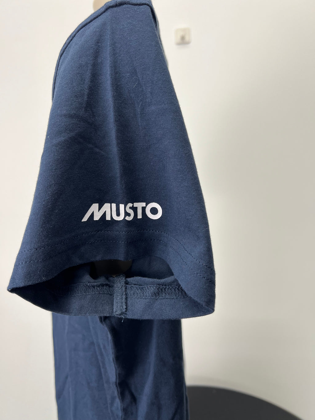Close-up of Musto logo printed on the left sleeve of navy blue t-shirt