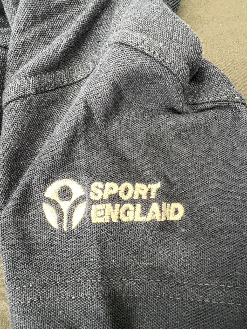 Close-up of Sport England embroidered logo on sleeve of navy polo shirt