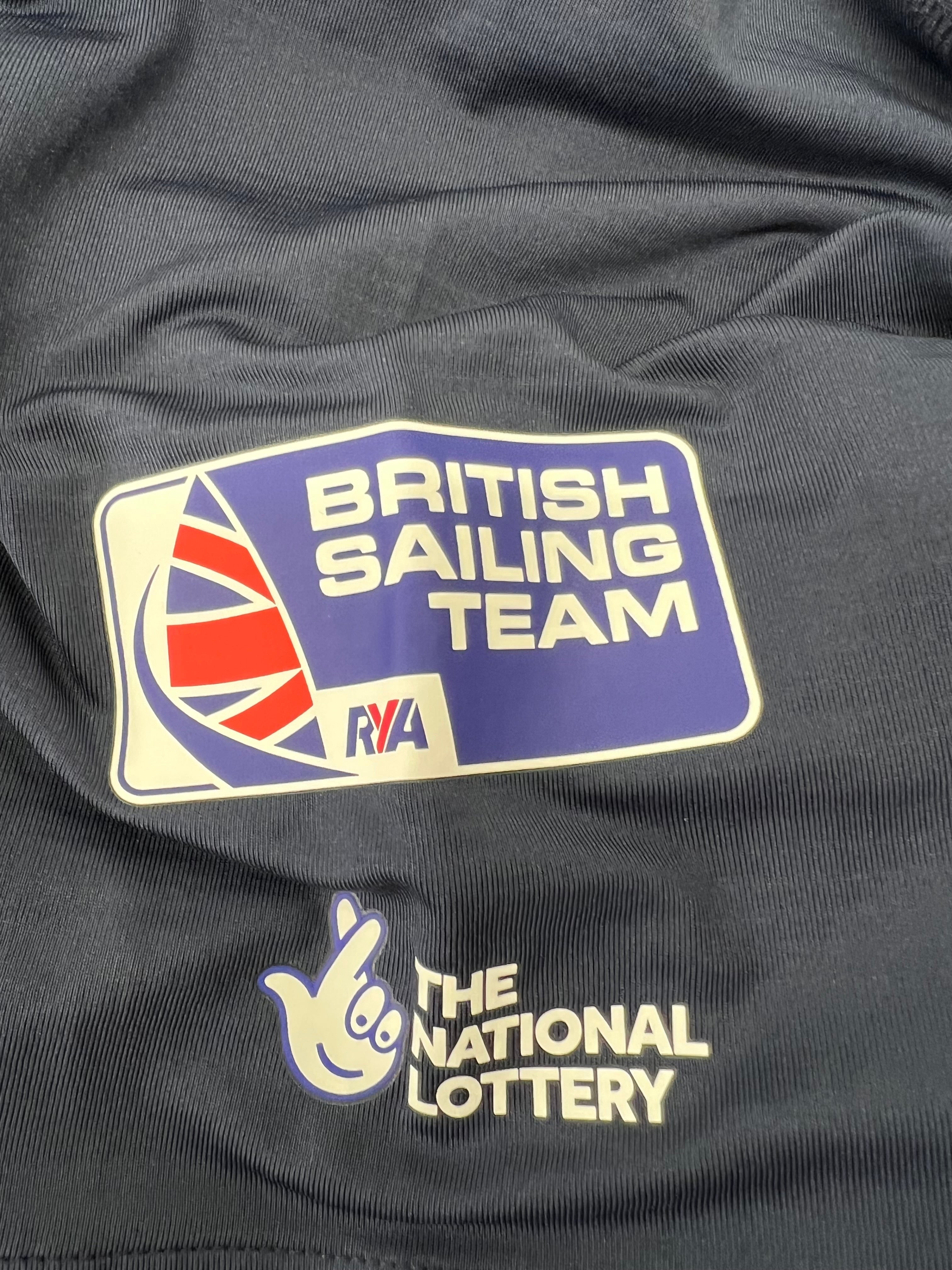 Close-up of British Sailing Team logo and The National Lottery sponsor logo on navy polo shirt sleeve