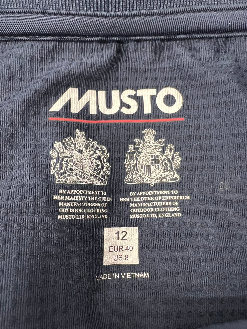 Close-up of Musto brand logo with Royal Warrants and size label inside shirt