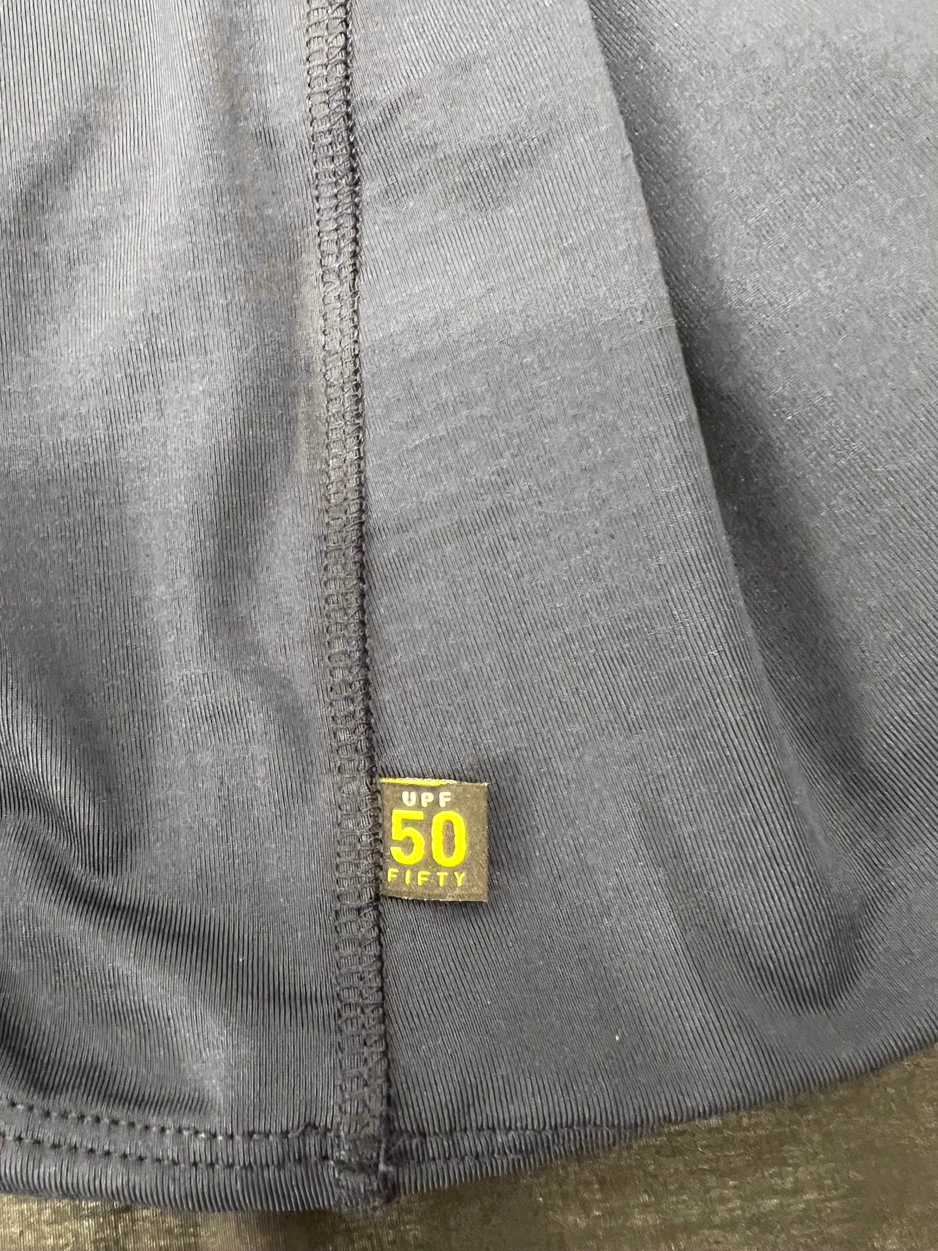 Close-up of UPF 50 sun protection tag sewn into side seam of navy blue polo shirt