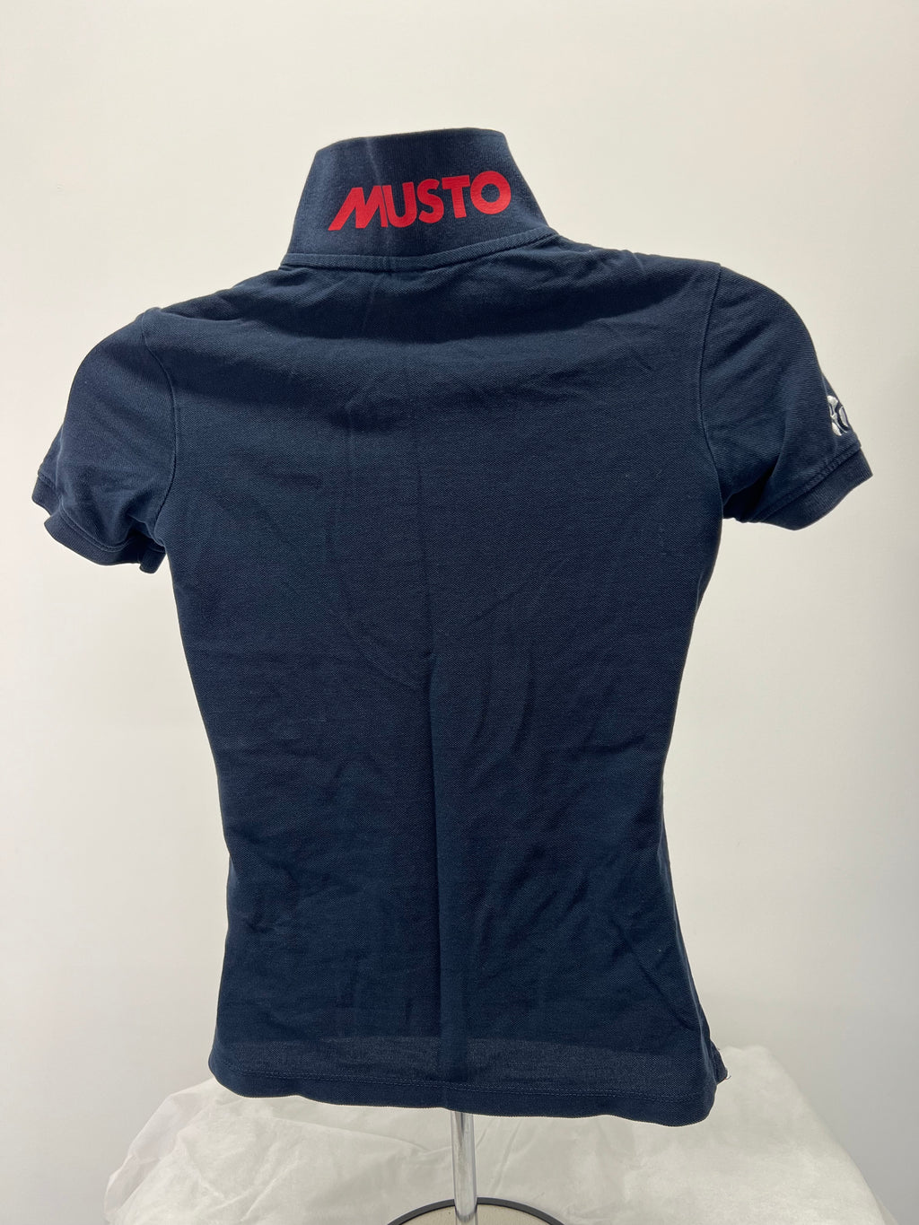 Back view showing Musto brand logo in red on raised collar of navy polo shirt