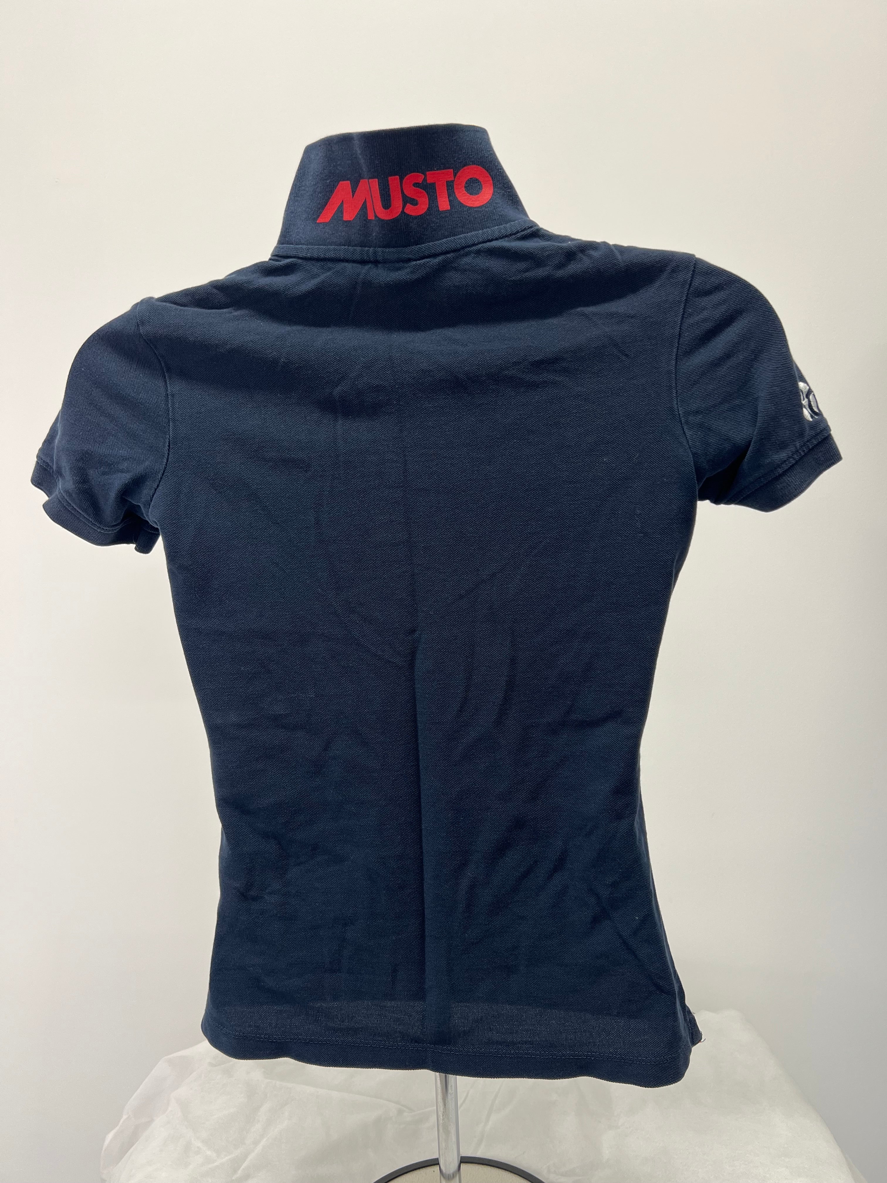 Back view showing Musto brand logo in red on raised collar of navy polo shirt