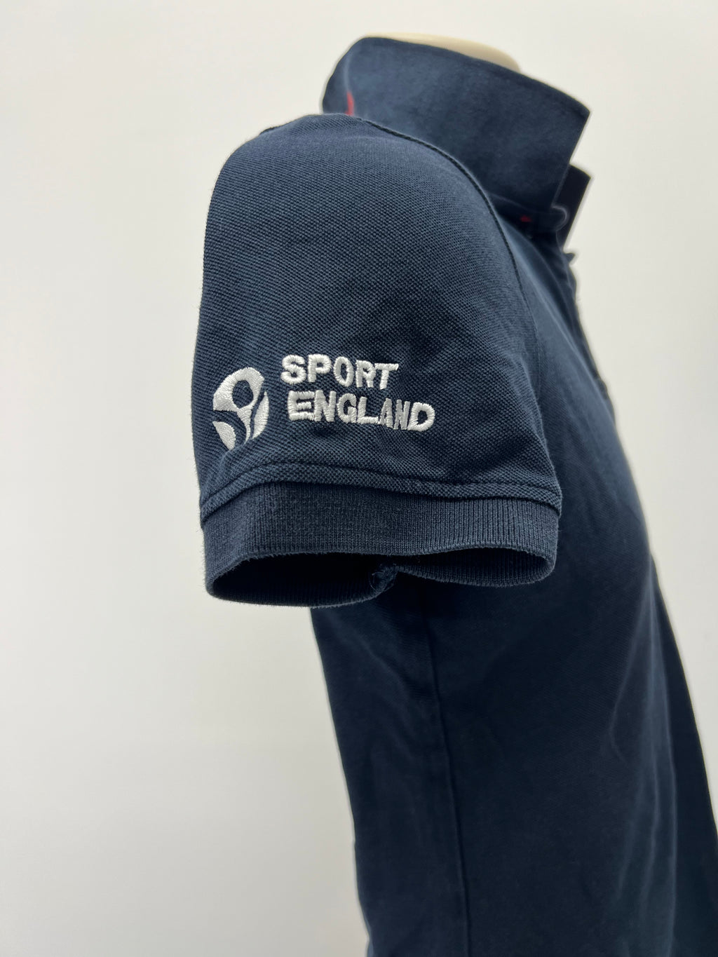 Close-up of sleeve with embroidered Sport England logo on navy polo shirt