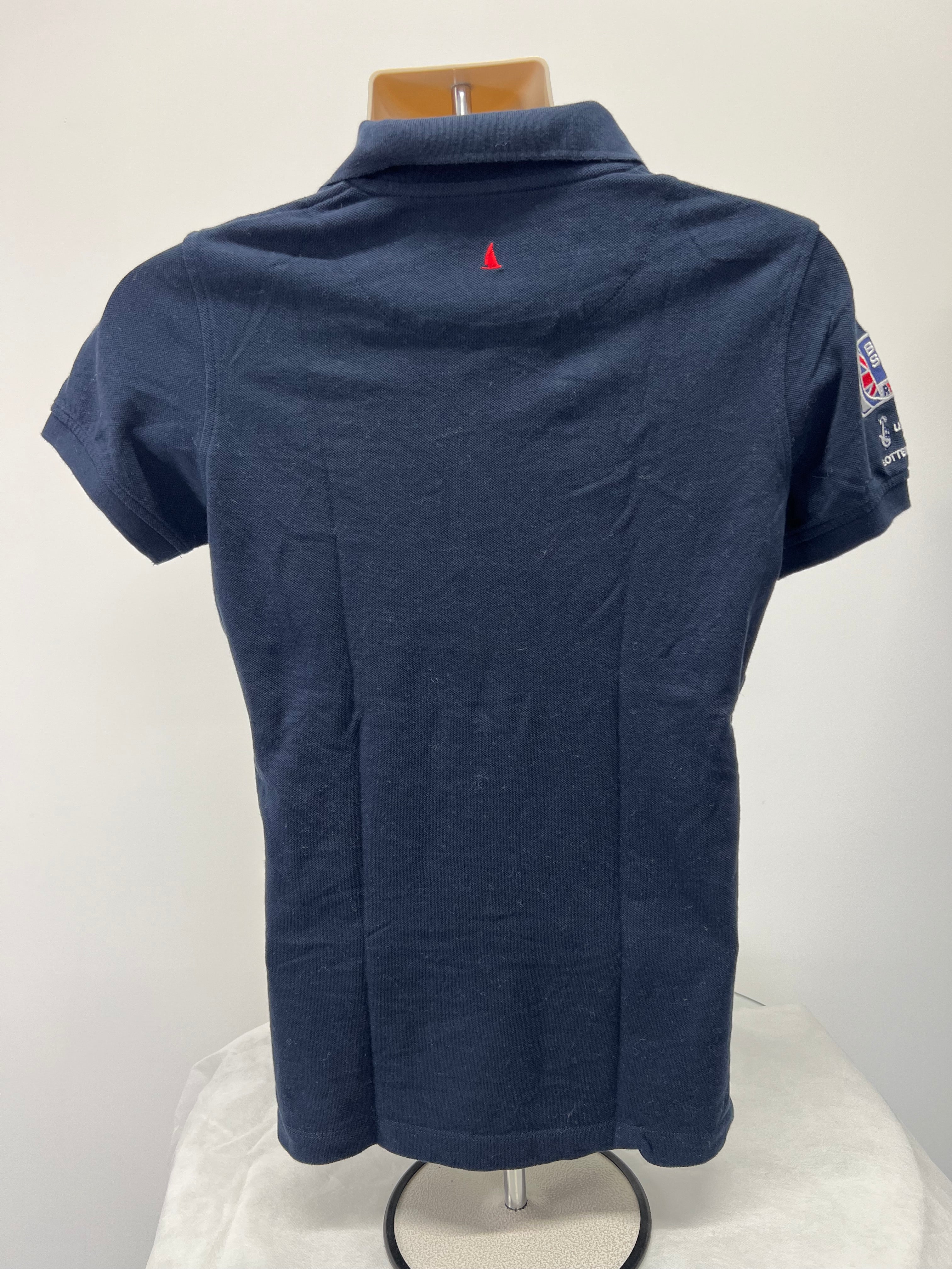 Back view of navy Musto polo shirt showing plain fabric and small red sailboat embroidery near collar