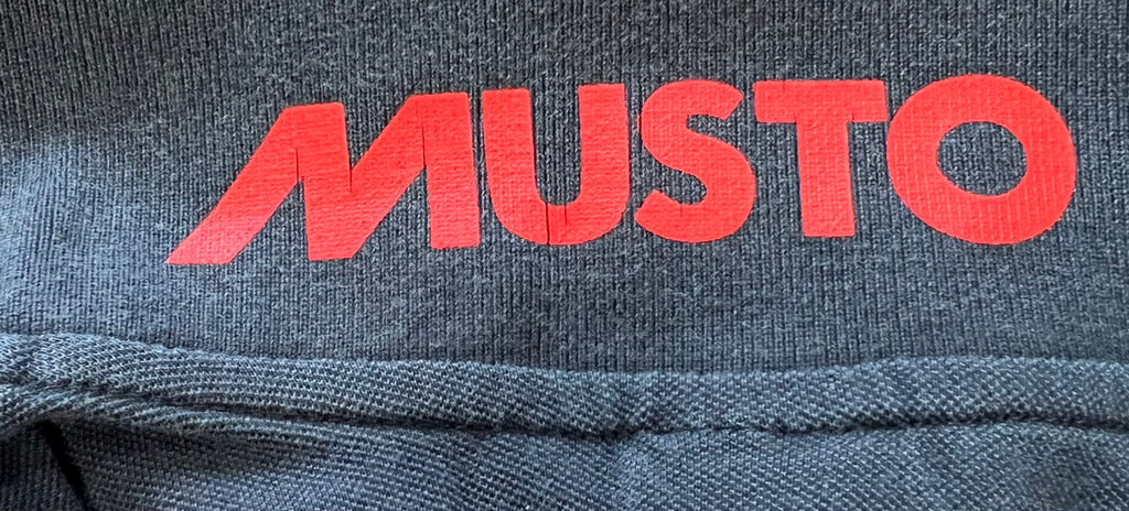Close-up detail of red Musto logo printed inside collar of navy polo shirt