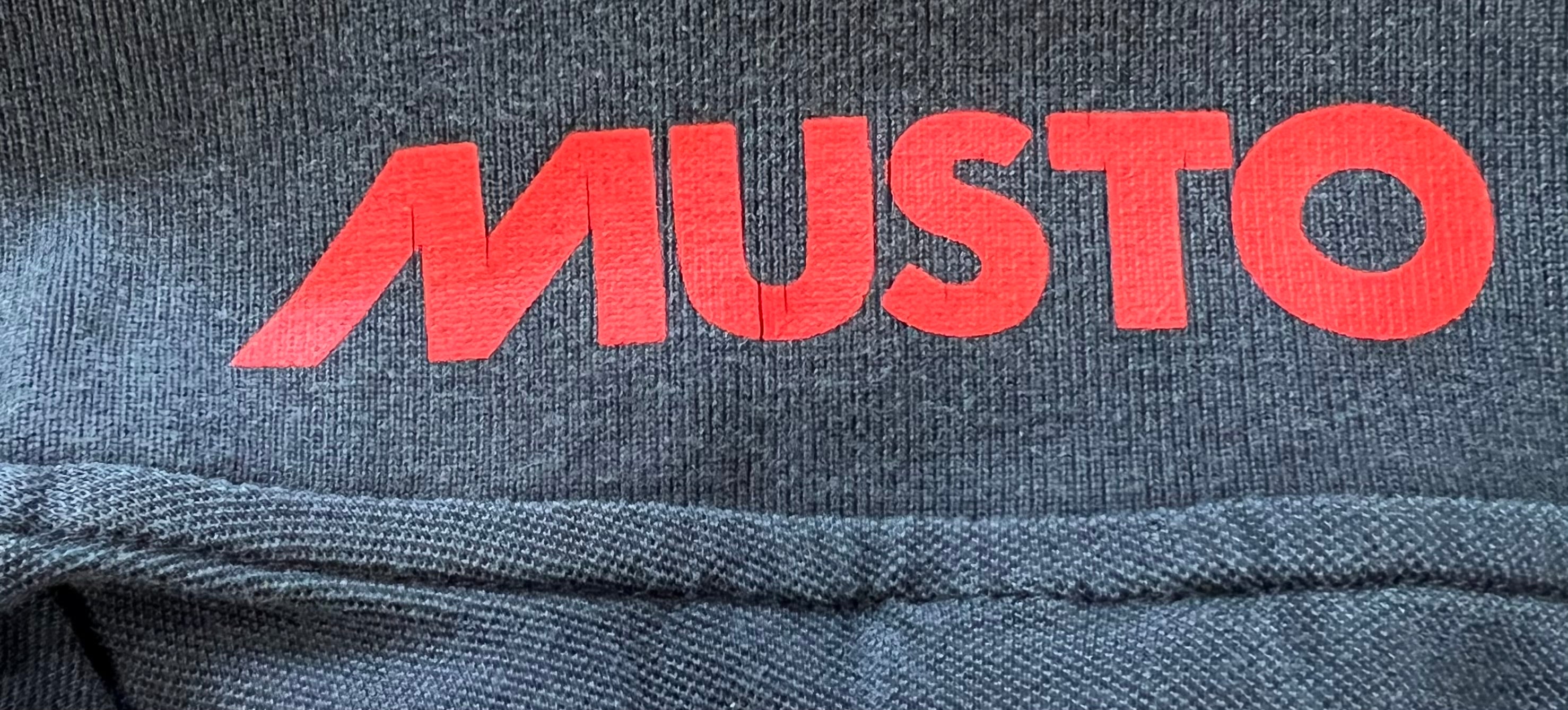 Close-up detail of red Musto logo printed inside collar of navy polo shirt