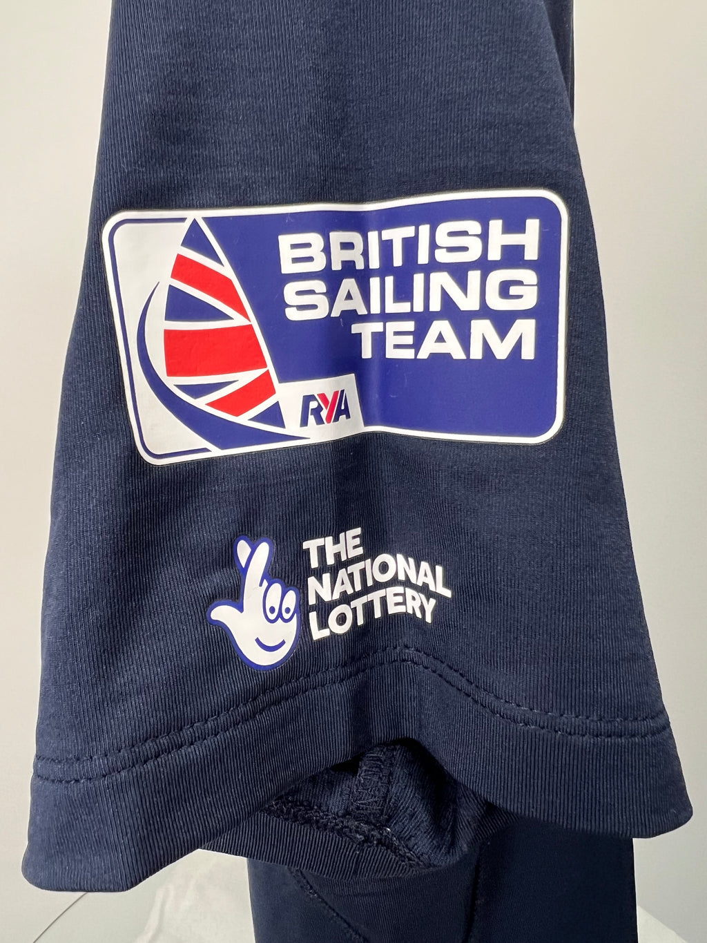 Close-up of sleeve logos showing British Sailing Team and National Lottery branding on navy polo