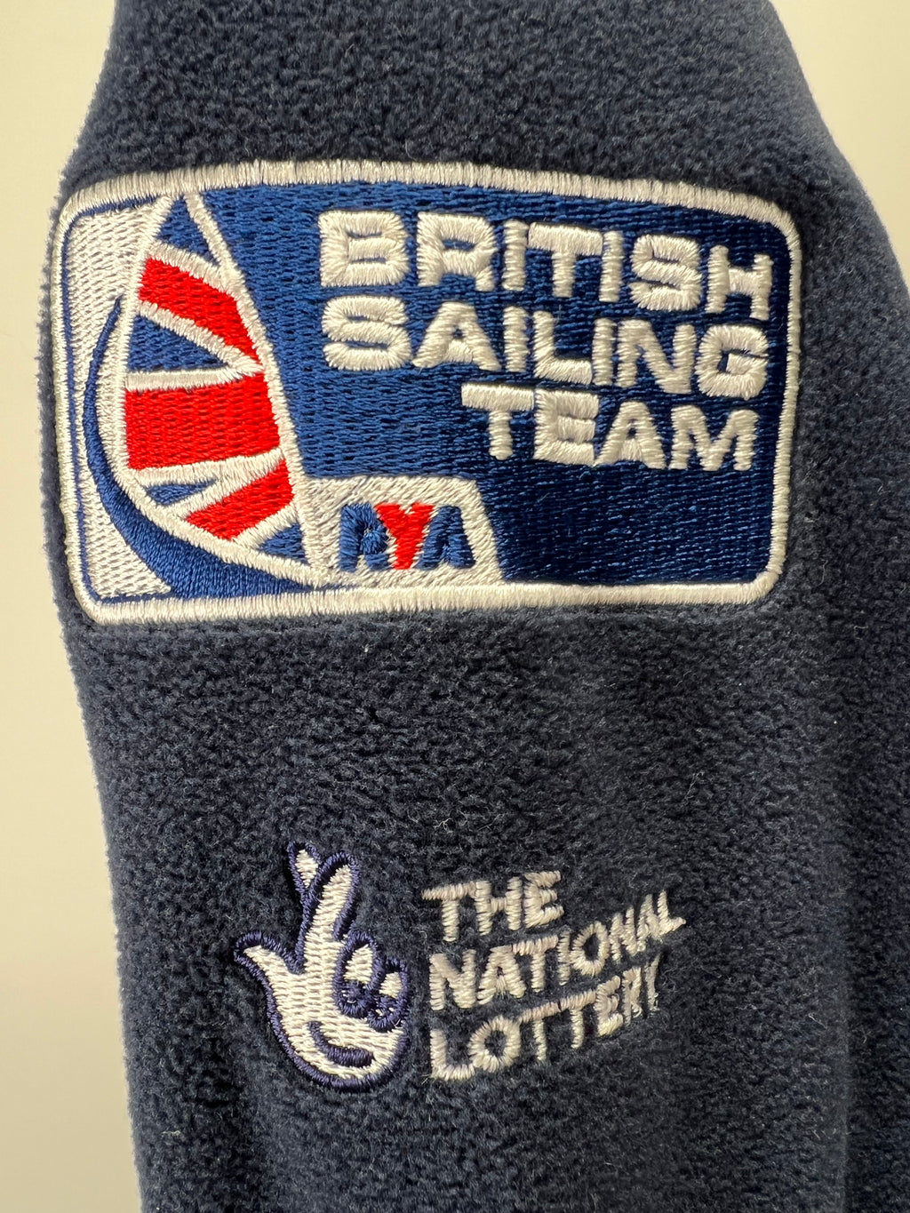 Close-up of British Sailing Team embroidered patch and The National Lottery logo on navy fleece