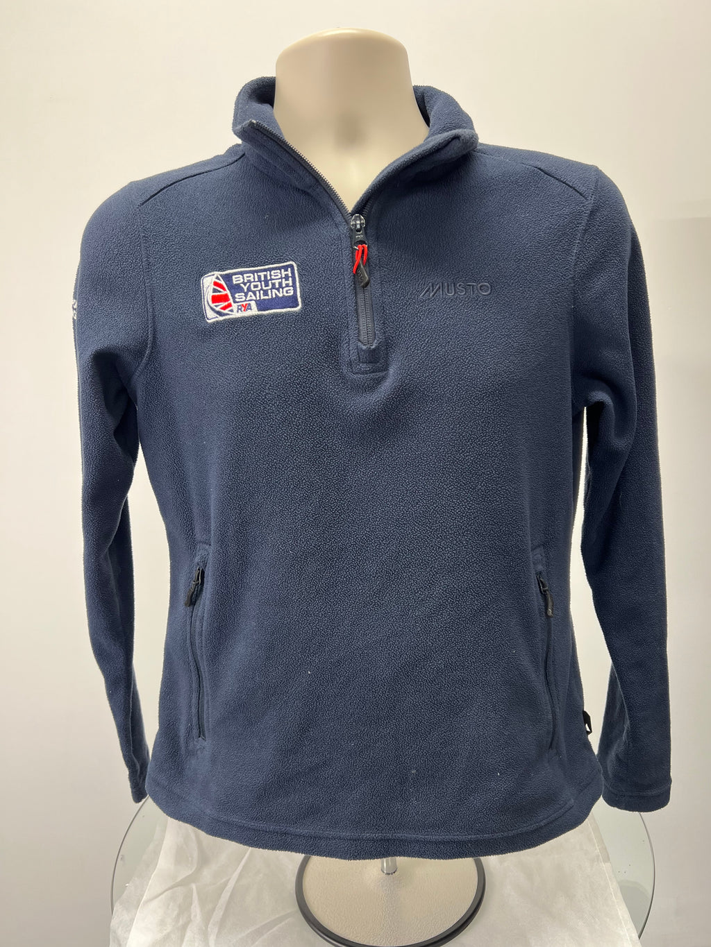 Front view of navy blue Musto British Youth Sailing half-zip fleece sweatshirt with zippered pockets and branded logo patches