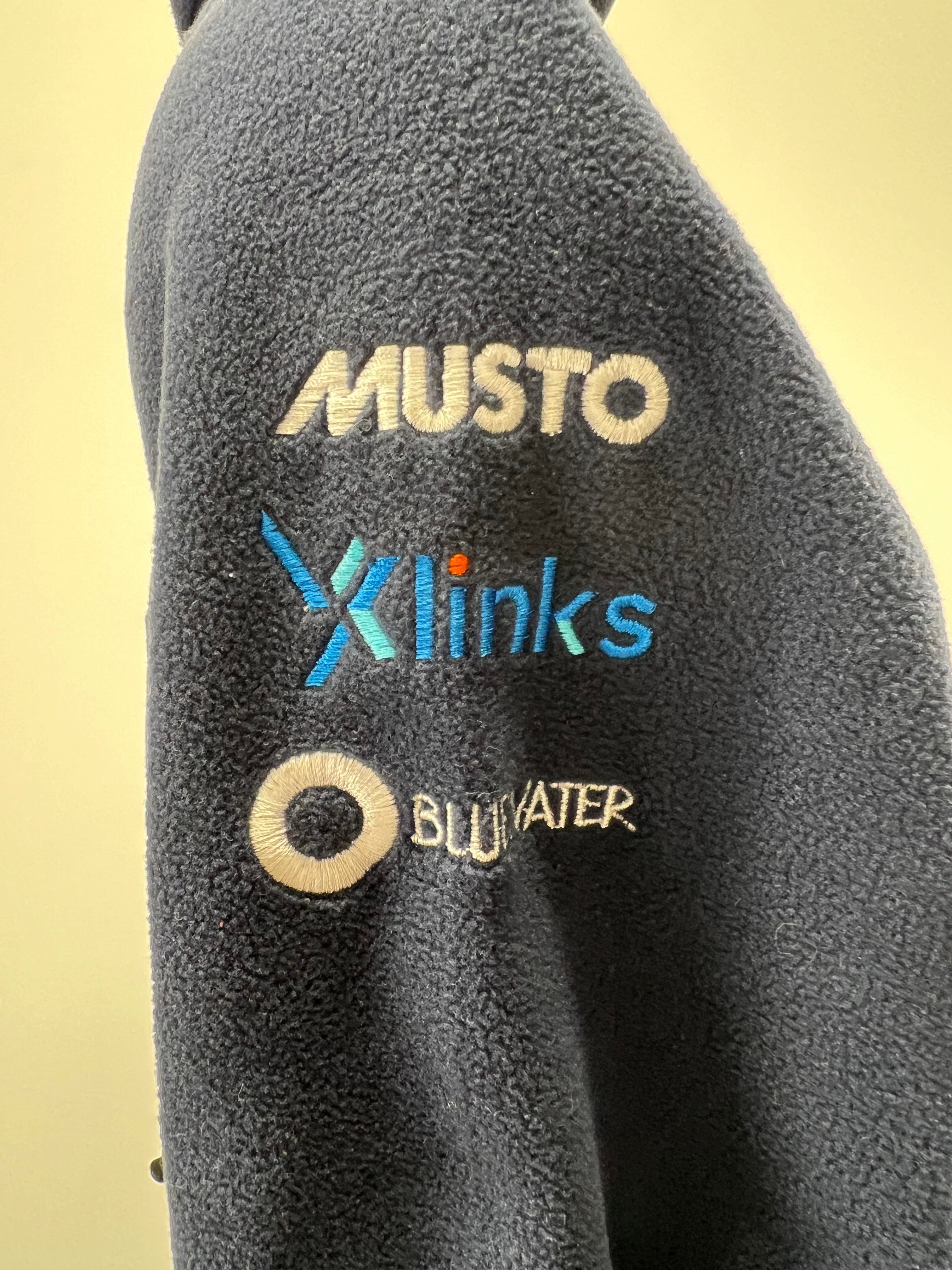 Close-up of embroidery on fleece sleeve showing Musto, Xlinks, and Bluwater logos