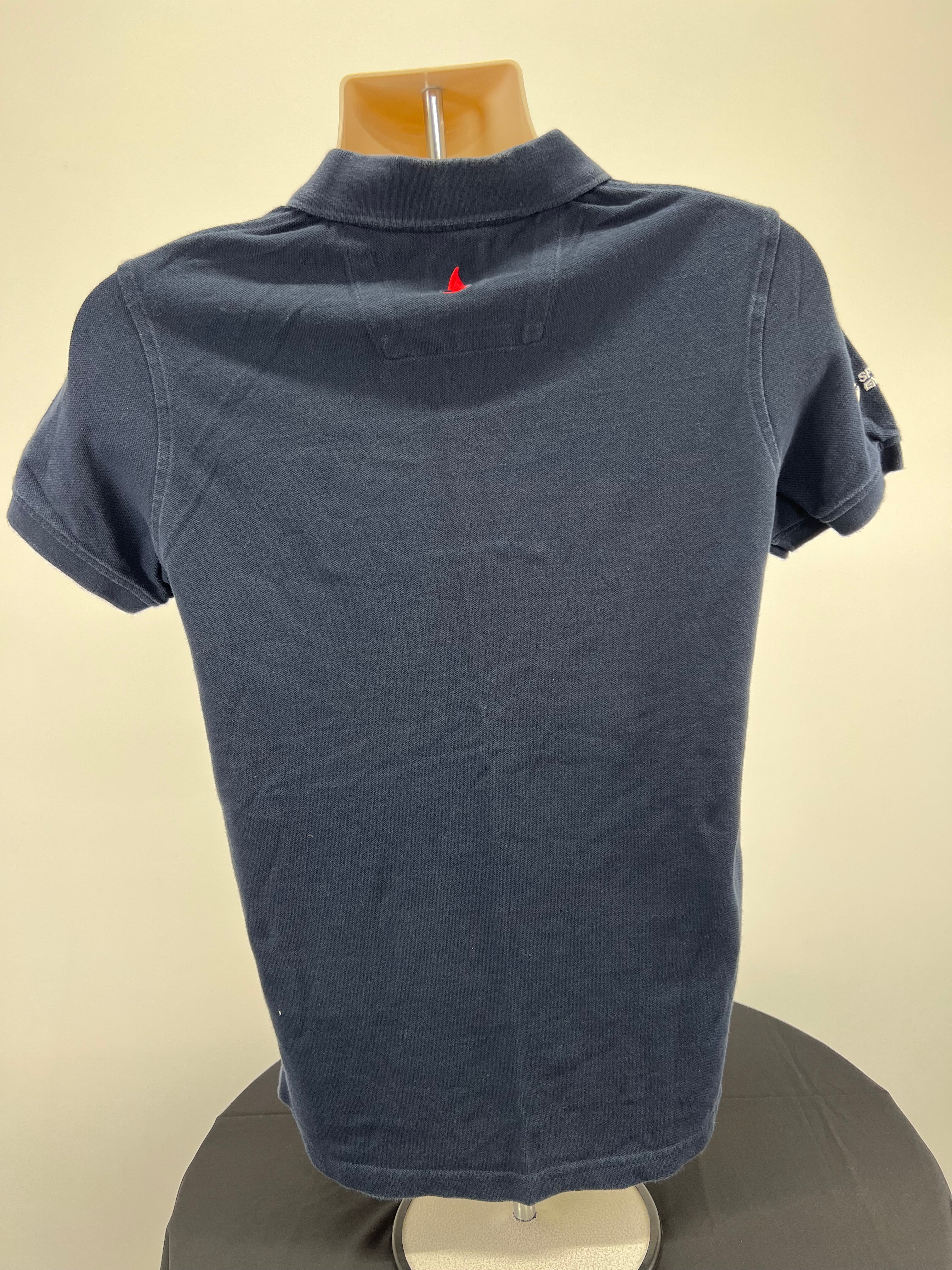 Back view of navy Musto polo shirt showing plain design with small red tab detail at collar