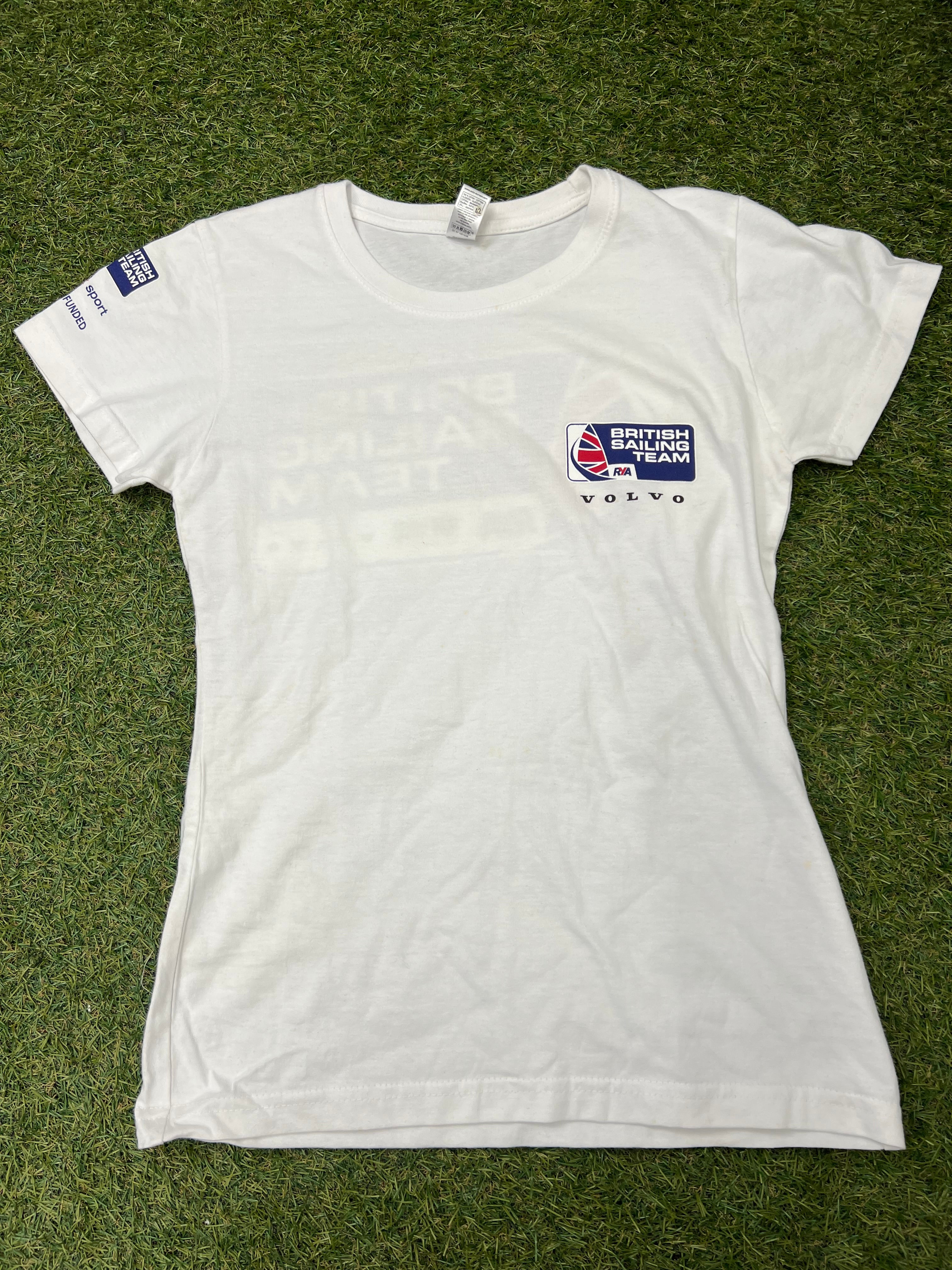 Front view of a white women's British Sailing Team t-shirt with small logo on chest and sleeve branding on grass background