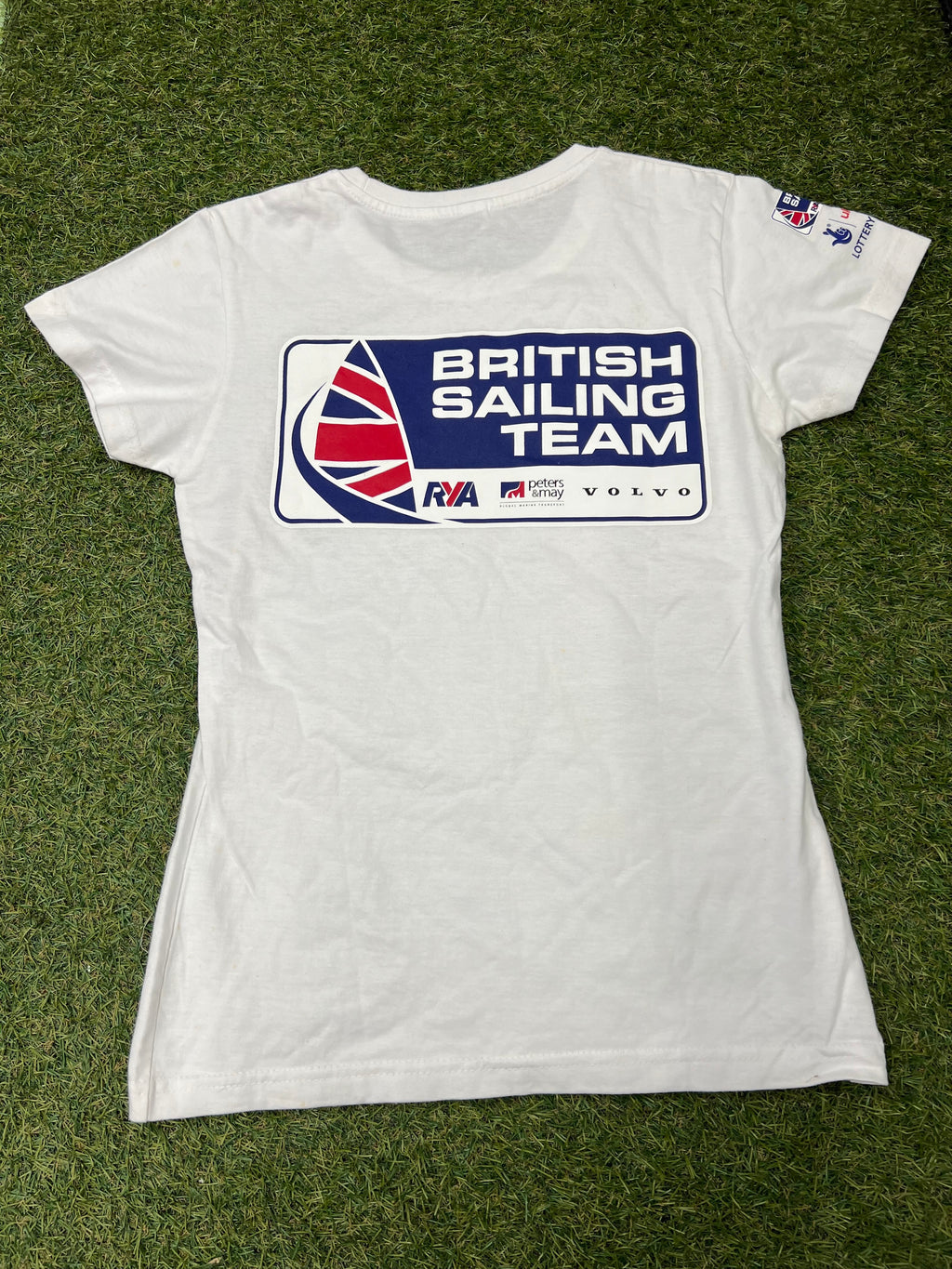Back view of the white women's British Sailing Team t-shirt showing large blue, red, and white team logo with sponsors on grass background